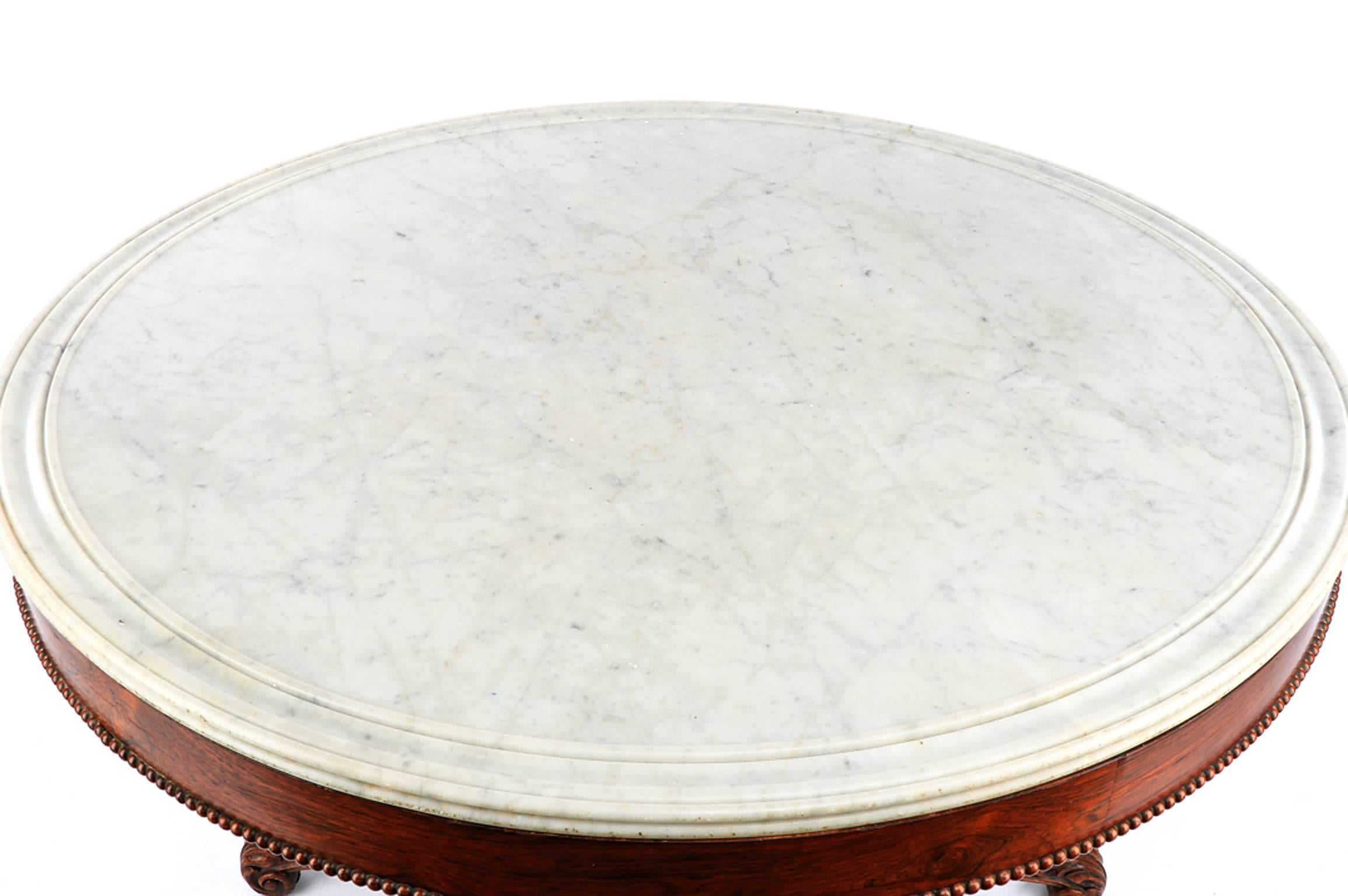 A mahogany veneered center table, the round white marble top with molded edge surmounting the mahogany veneered frieze with beaded edge over the base comprising a gadrooned column shaft with large ring turnings carved with leaves and c-scroll motifs