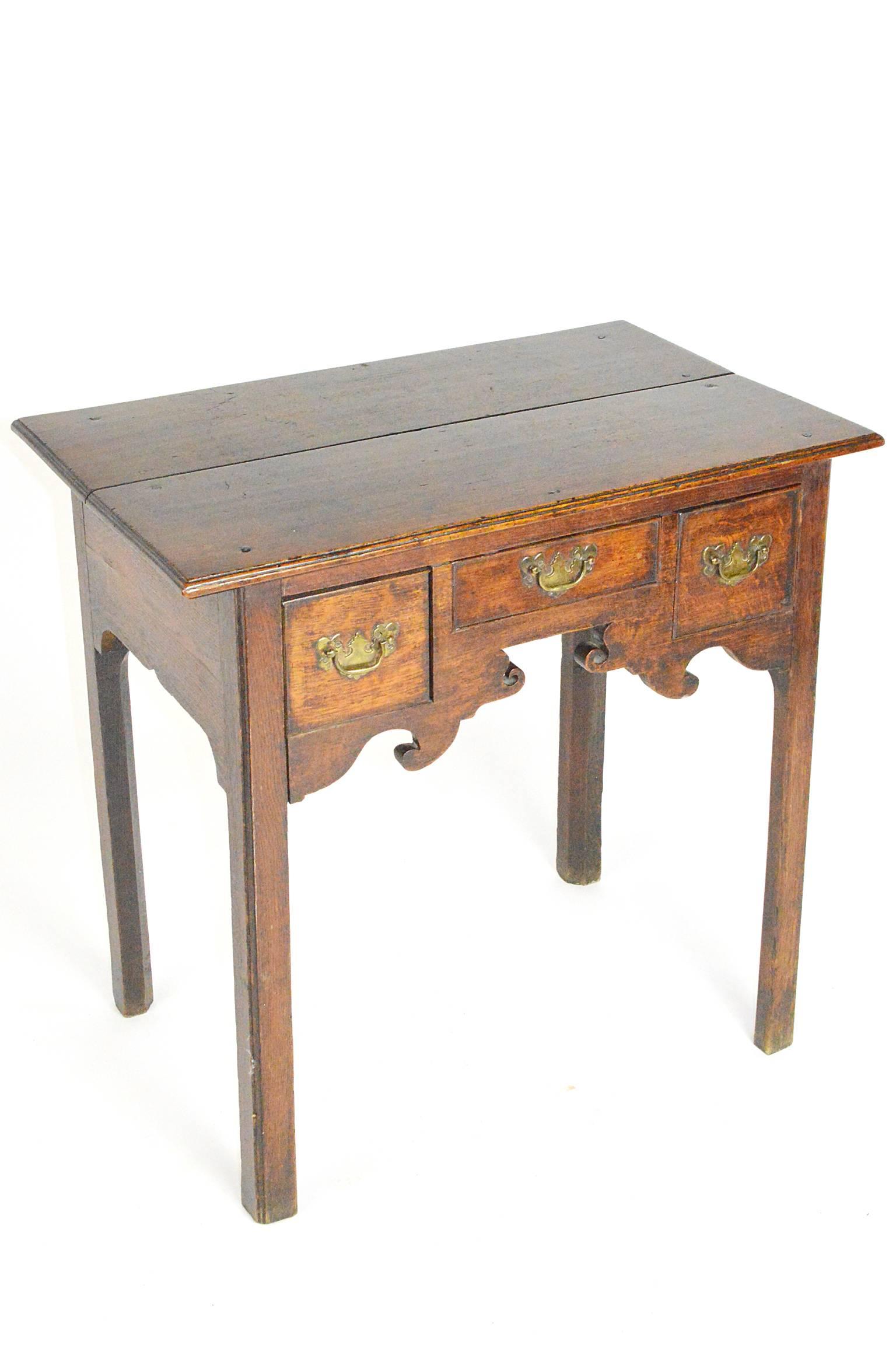 19th Century English oak country lowboy, its center having an elegant shaped frieze over straight legs. 