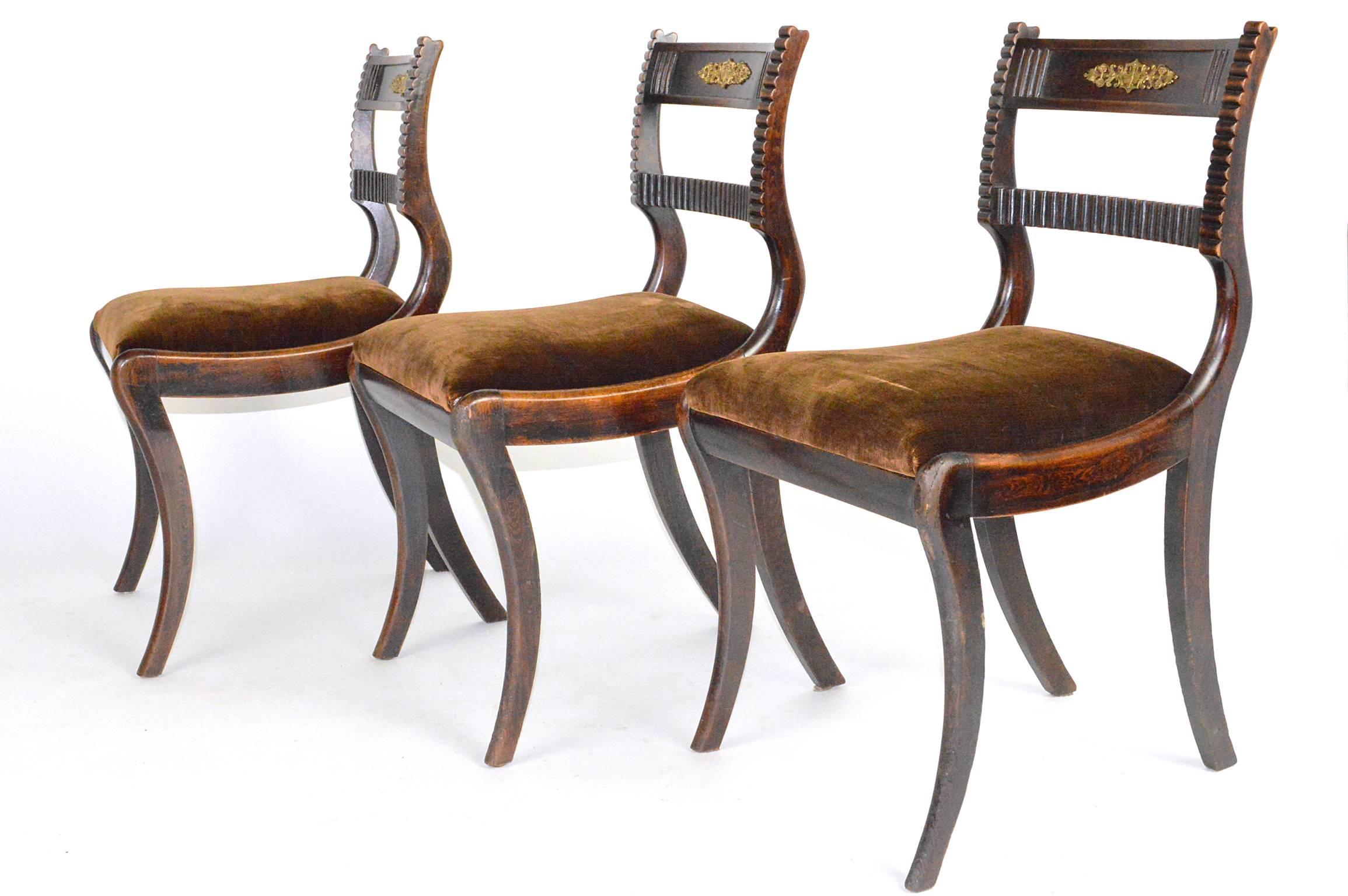 Set of six English Regency style mahogany side chairs with slip seat and saber legs. Each with a curved side rail and fluted center rail. With a center gilt bronze butterfly mount.