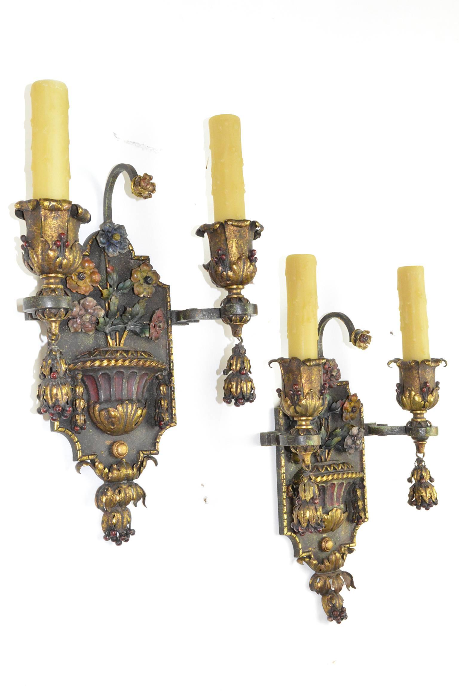 Pair of painted and gilt iron two-arm wall light sconces. Having cold painted decoration of urns and flowers.