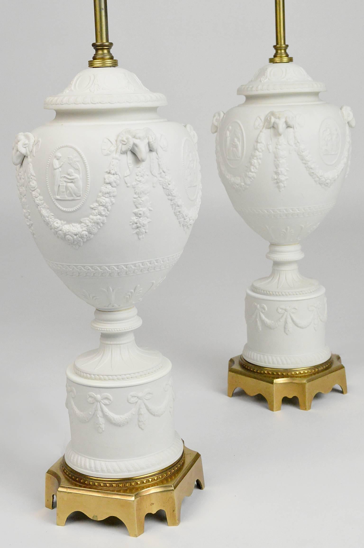 Pair of Warren Kessler American neoclassical style white parian bisque porcelain baluster-form lamps, each adorned with raised floral festoons emanating from rams heads among classical reserves, raised on brass plinth. Stamped 'Warren Kessler, NY'