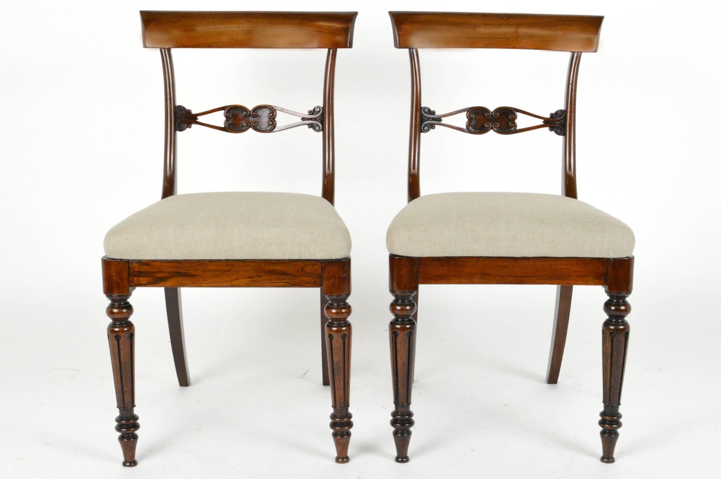 Set of four English Regency style rosewood dining chairs with intricately carved double loop mid rail above linen upholstered seat on turned fluted form front legs.