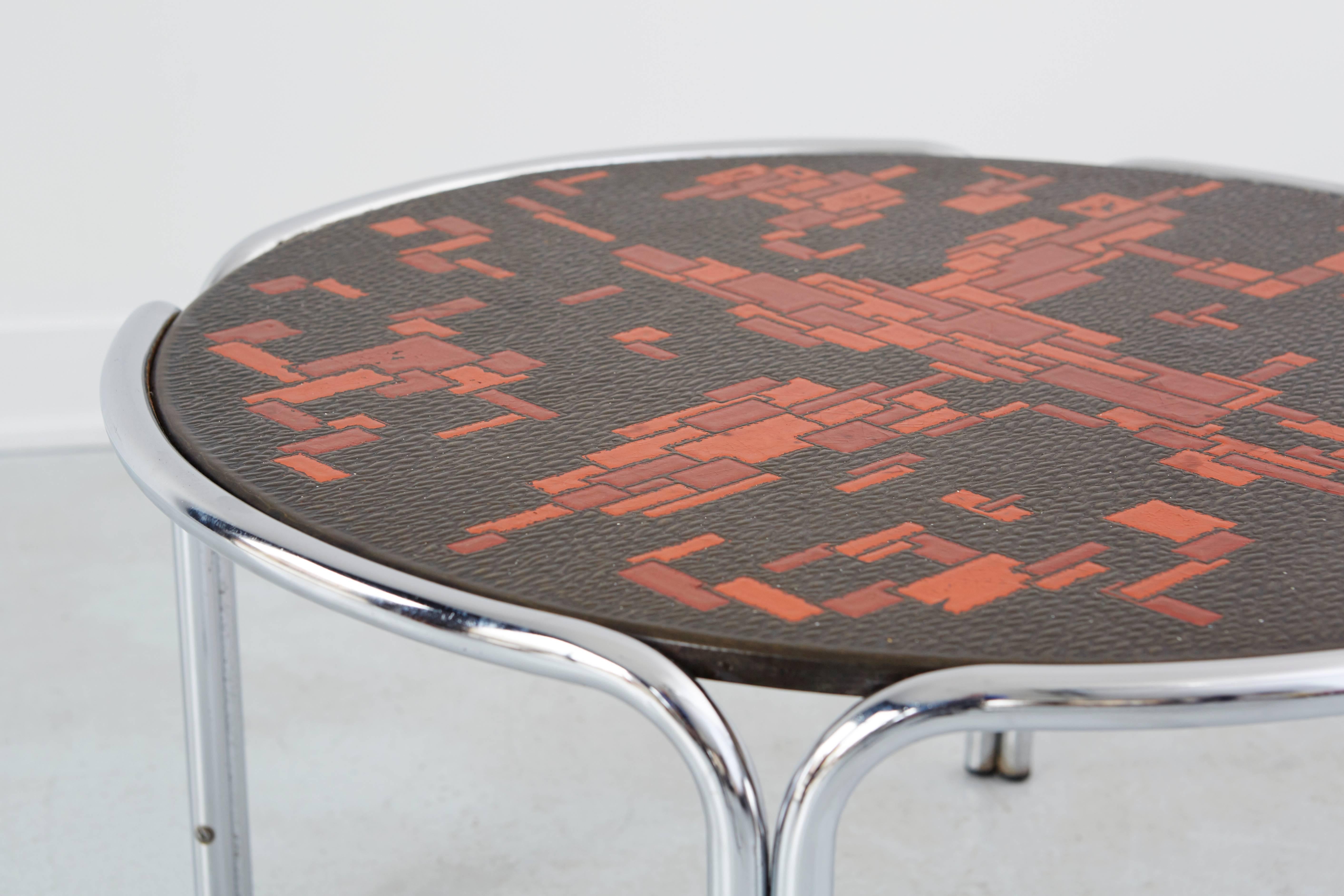 Mid-Century cocktail table attributed to Roger Capron. Tabletop is an abstract mosaic mandarian orange and blood red geometric design with feathered black background. Tabletop is balanced by chromed steel legs. Table is from London, England, circa