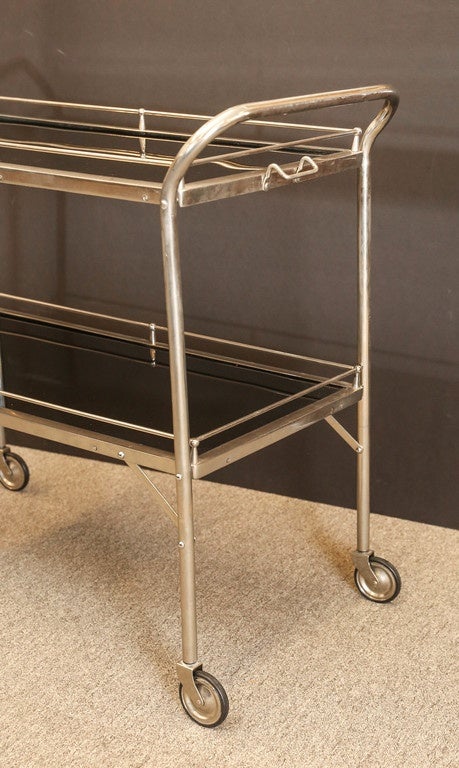 Two trays surrounded by the thin chrome tubing, to protect items from falling down while moving the cart. The trays are attached to the wider tubing, that is curved on top to create handles. Four legs have weals attached to them.

36”W x 15”D x