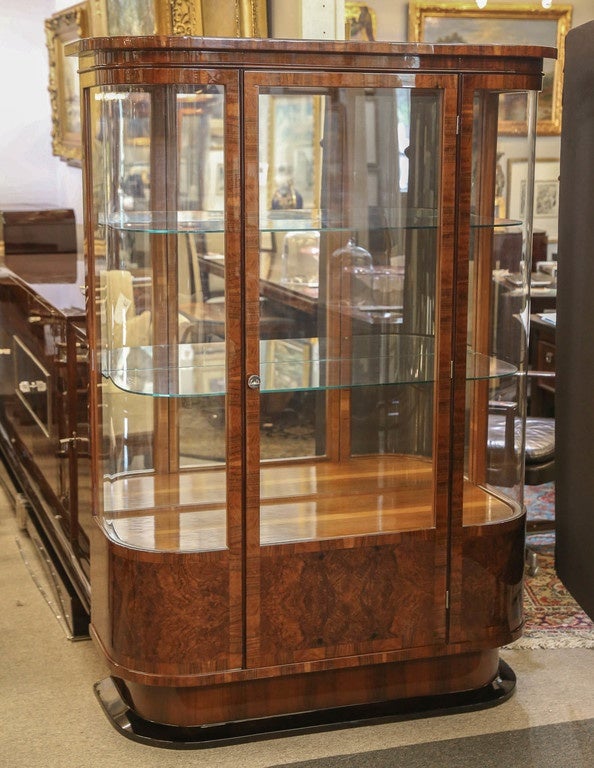 Walnut veneered, shaped display/vitrine. One tall door fitted between curved glass sides. Hinged keyed door with glass. Two glass shelves. Nicely trimming top, and resting on sloped base. 

  Restored

 48”W x 18.5”D x 67.5”H