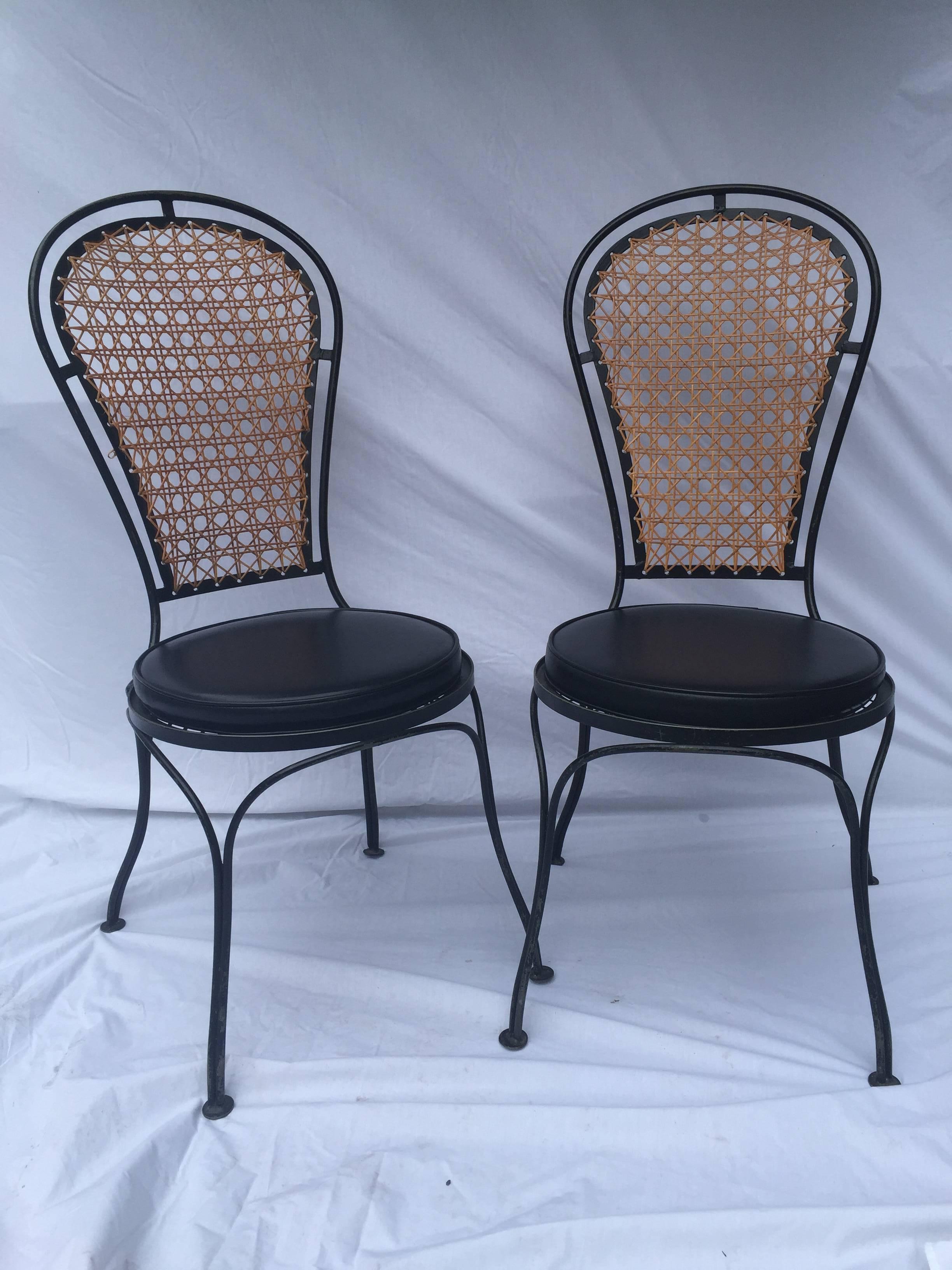 Pair of vintage iron balloon back style chairs with a woven cane back. Definitely in the style of Salterini. More measurements: Seat is 18.5 inches high with the cushion, the width and depth at the feet is 18.5 inches by 18.5 inches.