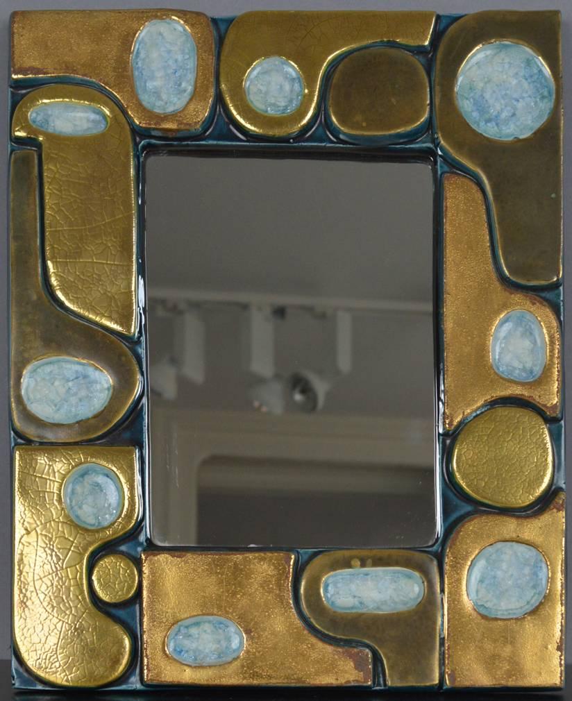 Glazed ceramic mirror by François Lembo, Vallauris, France, 1960s. Rare and beautiful glazed ceramic modernist mirror composed of enameled ceramic shapes in a blue and gold radiant, adorned with a mirror. The back is covered in green felt.

In