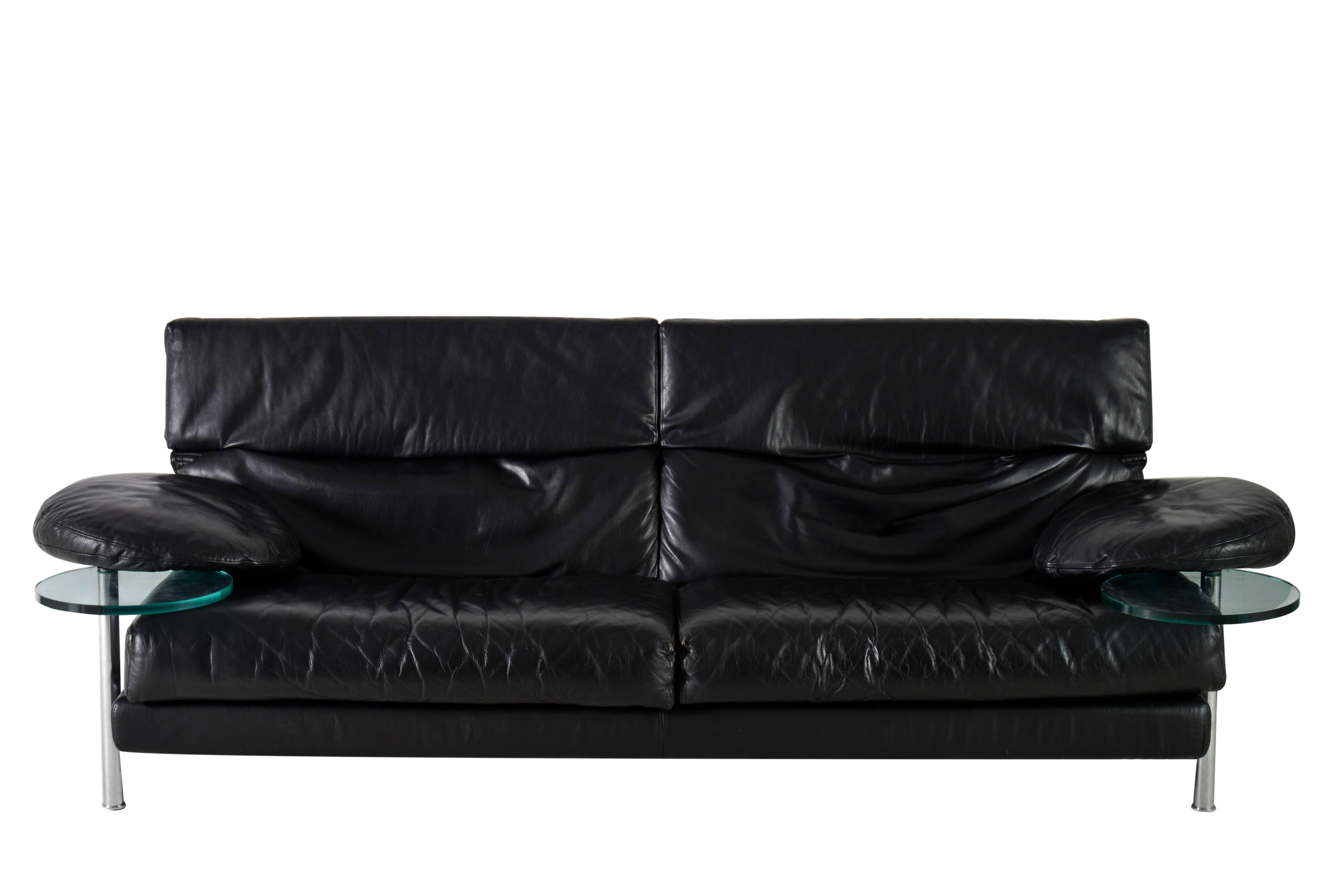 B&B Italia Arca sofa with right and left armrest provided with transparent glass serving tables which swing out from under the armrest. Framework made of structural steel embedded in cold foamed polyurethane and perforated black leather. The