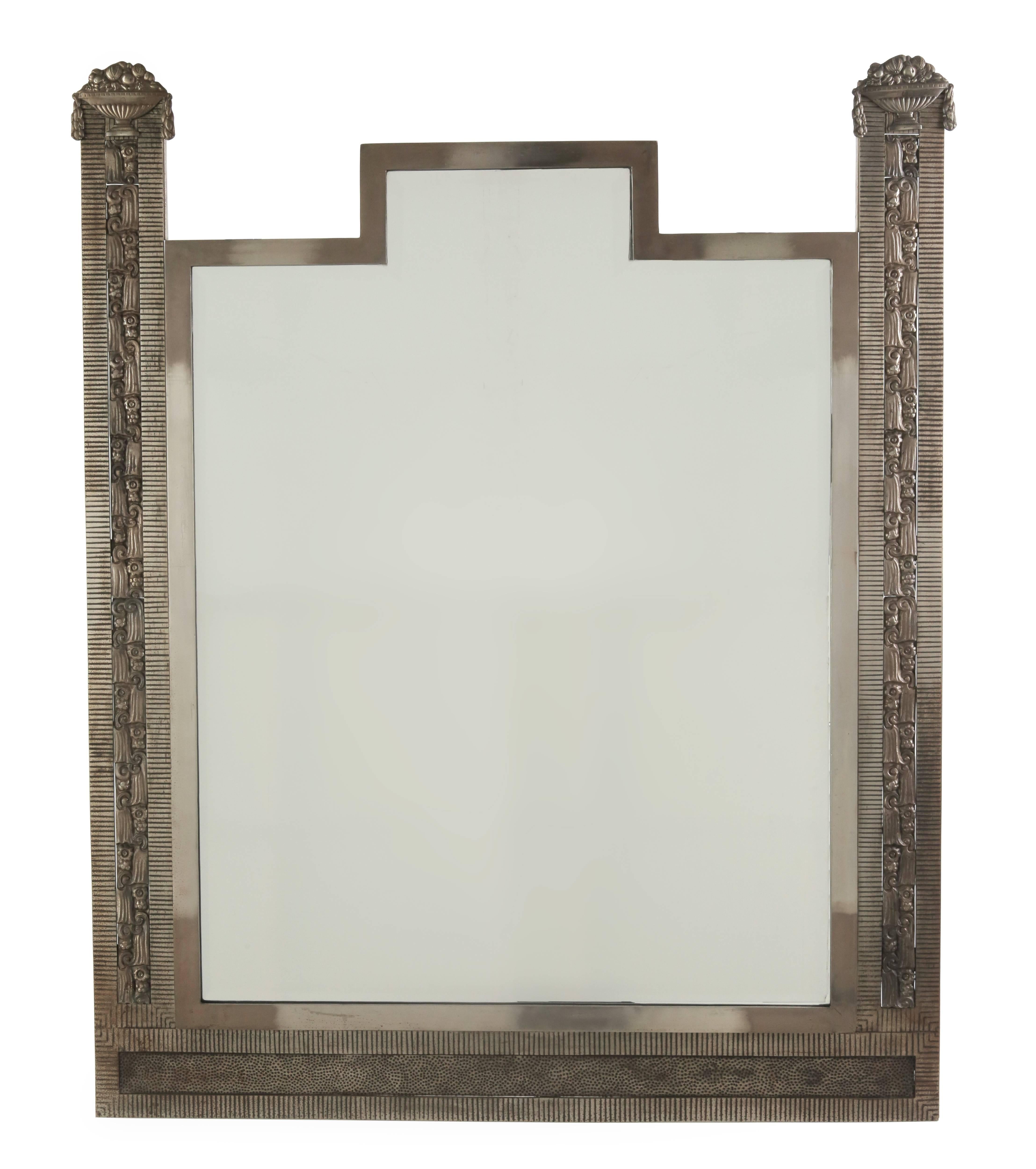 A large hand-hammered nickeled iron, fine French wall mirror. Floral motif with fruit urn design flanks sides and brings to view a typical shaped beveled mirror inset.