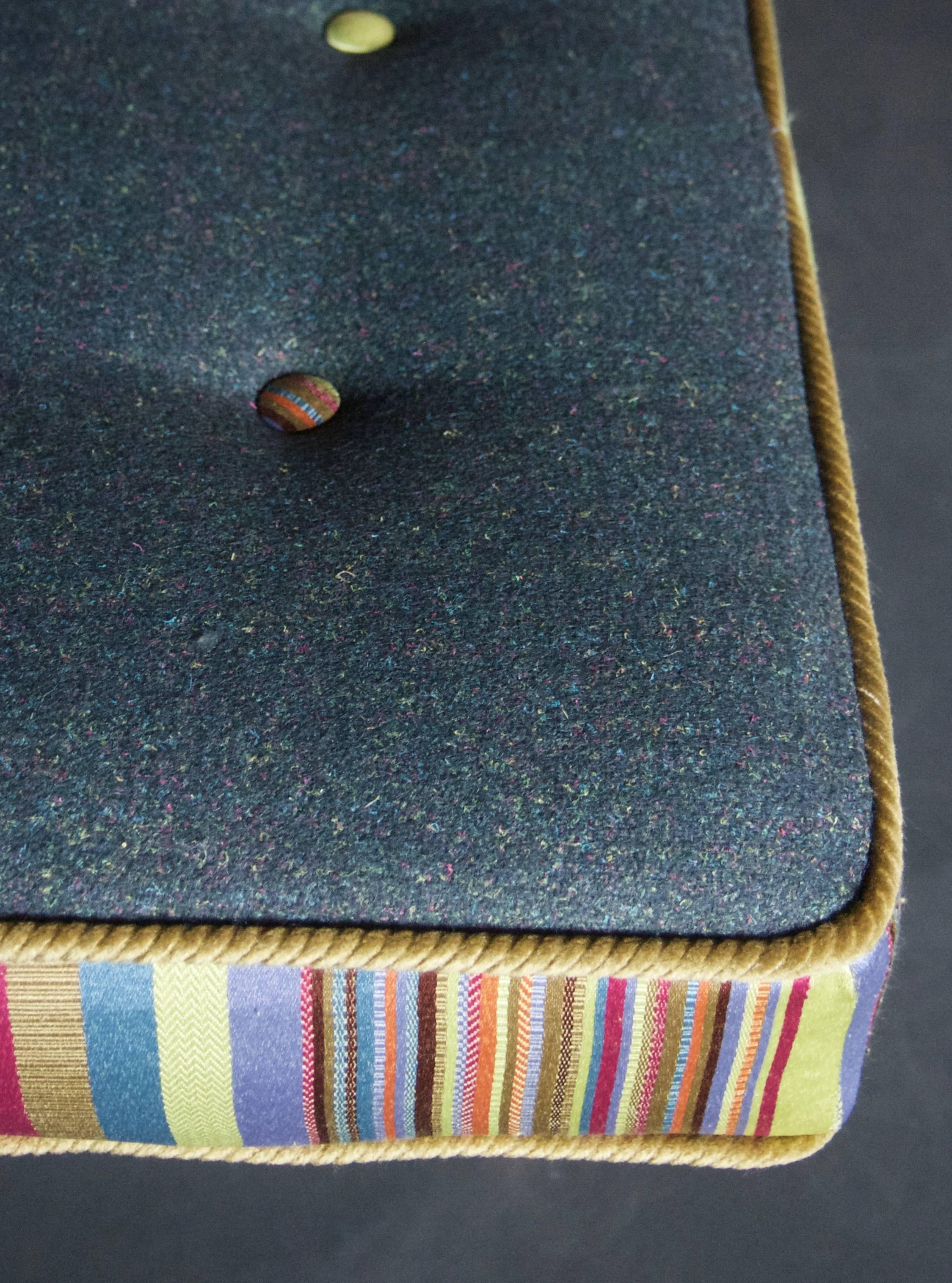 This upholstered bench is handmade using traditional European upholstery techniques, and tufted with 14 colorful buttons. The seat top is charcoal gray flecked with colorful threads, surrounded by a bold vertical stripe on the boxing (side panels).