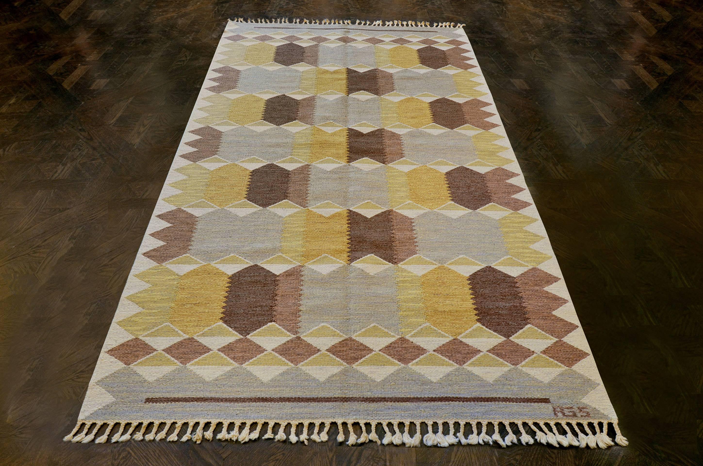 This vintage handwoven Swedish rug has an overall field of tonal brown and yellow serrated and angled lozenges forming a whimsical checkered lattice. Signed by the original artist.