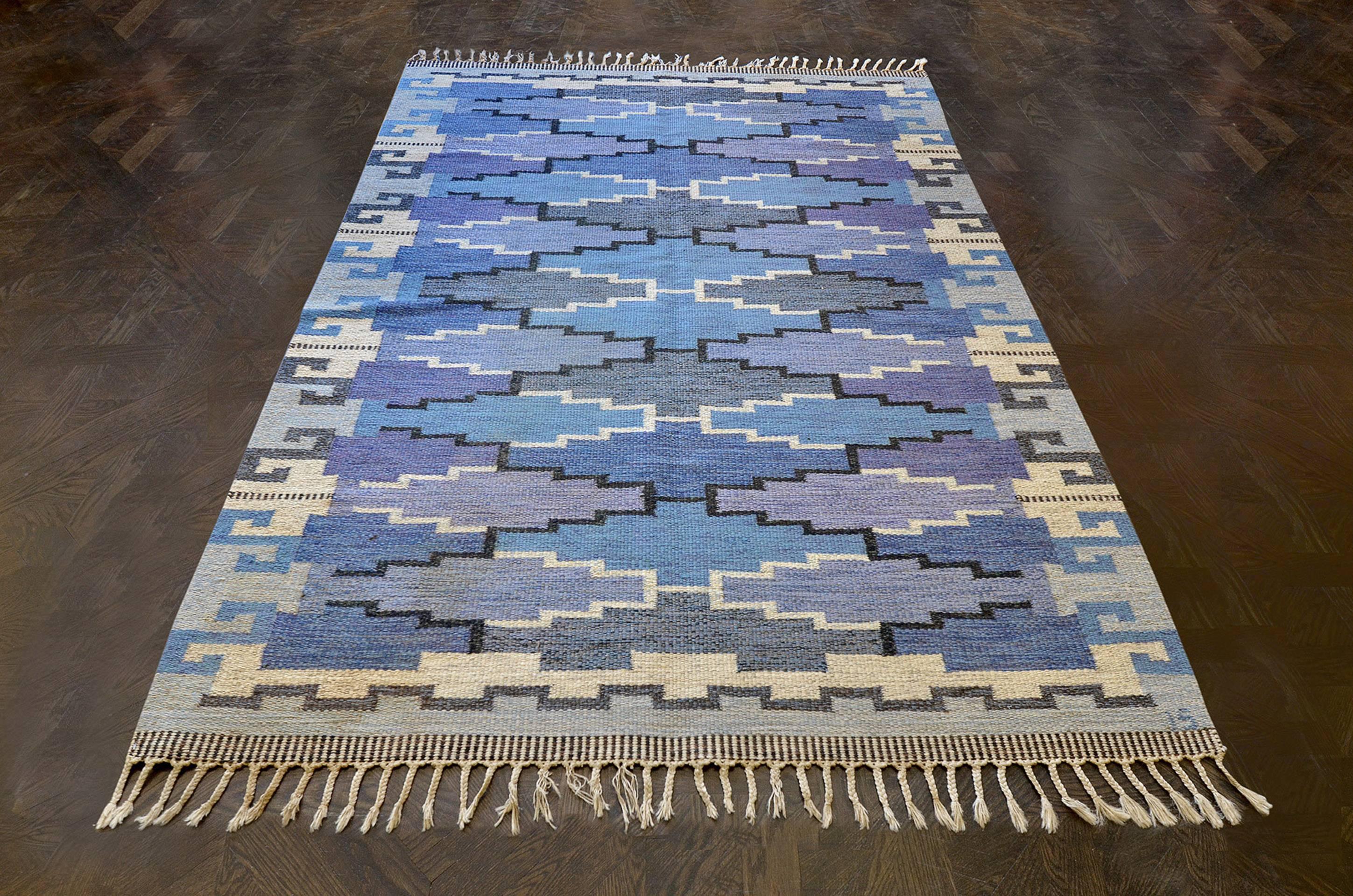 This vintage handwoven Swedish rug has a cool tonal overall field with oblong stepped lozenge lattice, in a complementary stylized geometric “S-motif” border. Signed by the original artist, Ingegerd Silow.