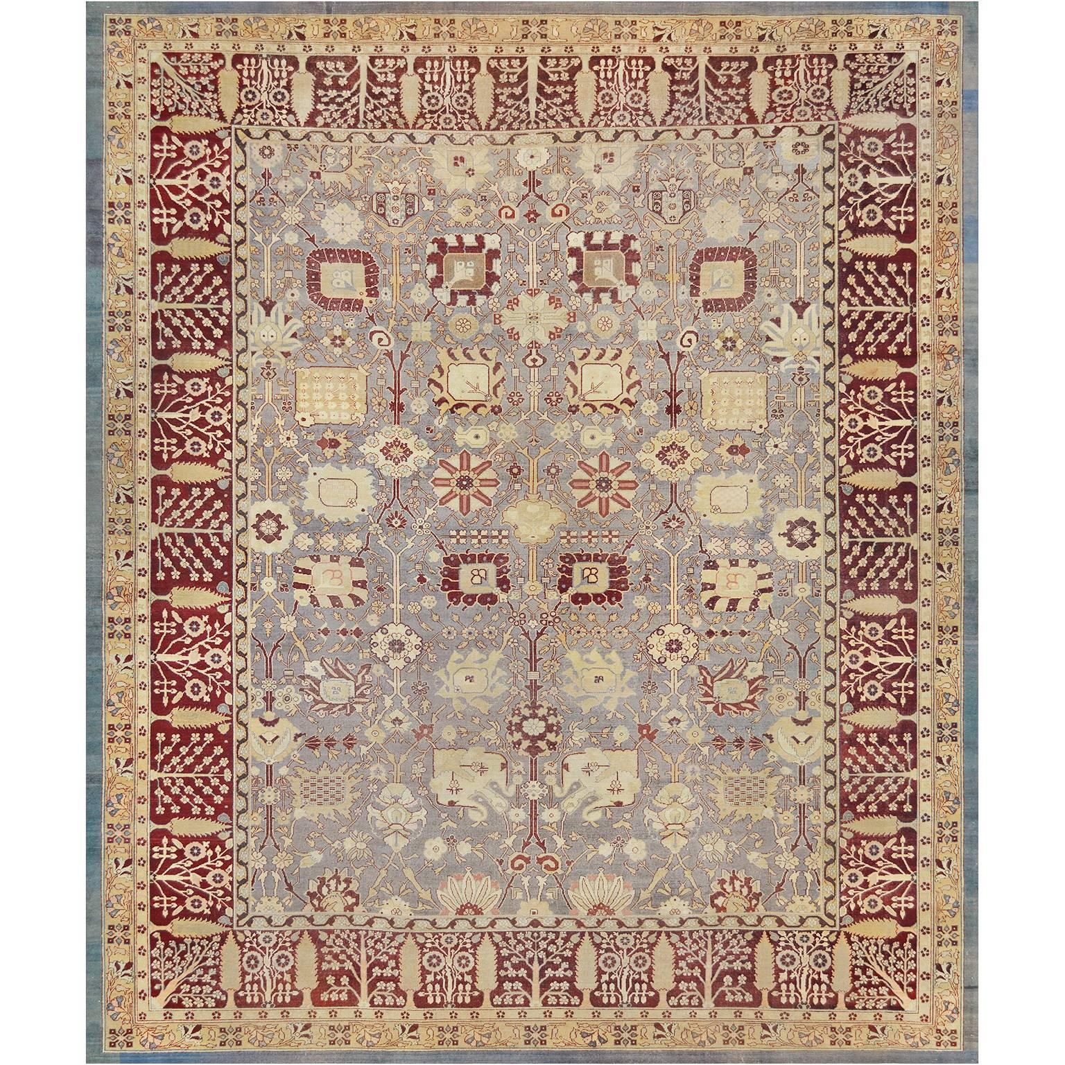 This traditional handwoven Indian Agra rug has a shaded slate field with overall counterposed design of elegant palmettes issuing scrolling angled floral vines, in a regal burgundy red border of cypress trees and flowering plants, between ornate