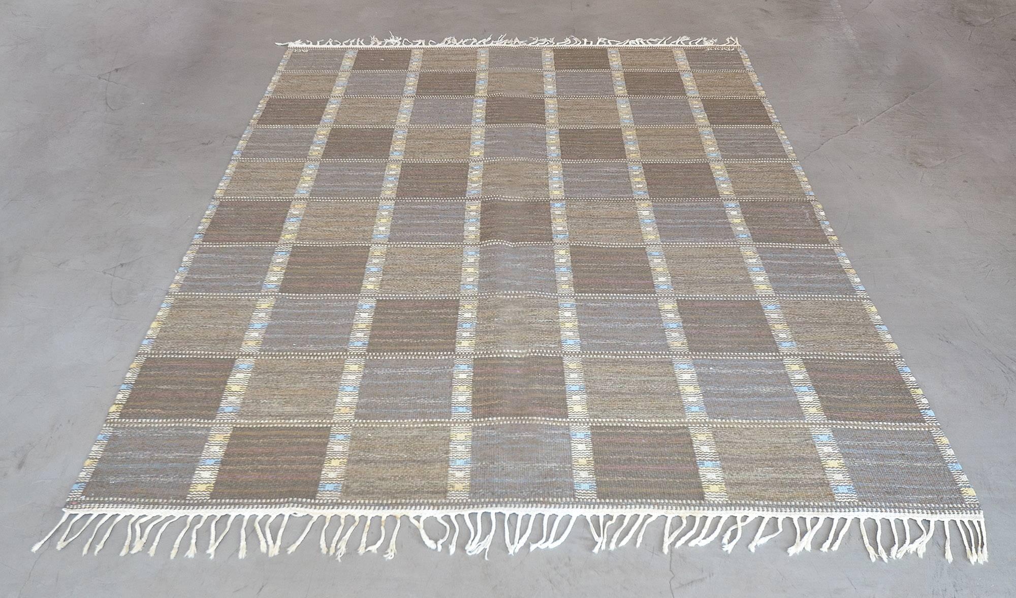 Ce tapis suédois vintage tissé à la main présente un champ à carreaux composé de rangées diagonales taupe ton sur ton, séparées par des rayures tribales. Signé par l'artiste original et l'atelier.

À propos du maître tisseur :
Le paradigme
