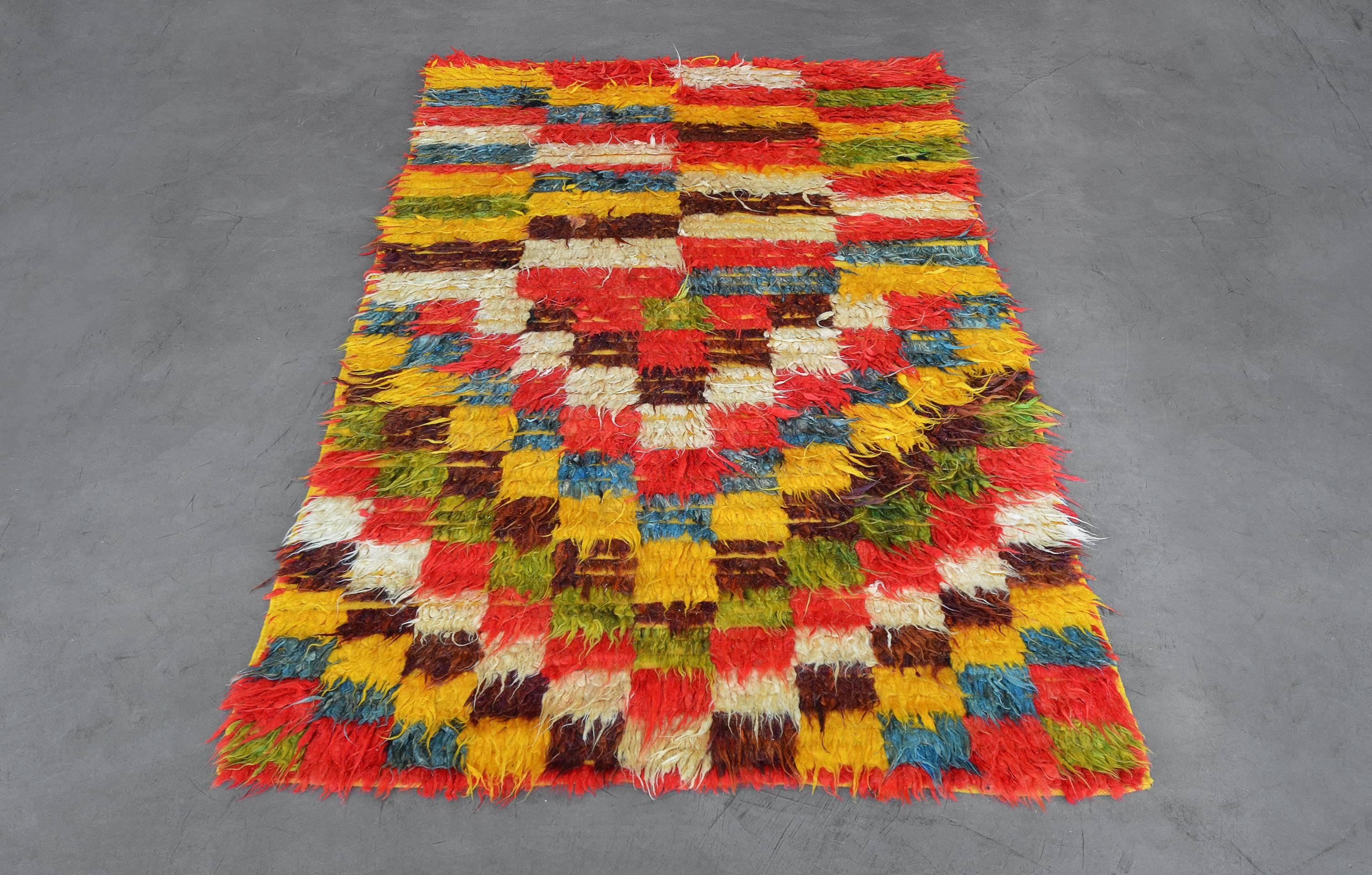 This vintage 1970s deep-pile Moroccan rug has a polychromatic checkerboard field of tufted coral-red, light-green, shaded blue, ivory, chocolate-brown and golden-yellow, the lower half of the rug with horizontal alternating linked panels, the upper
