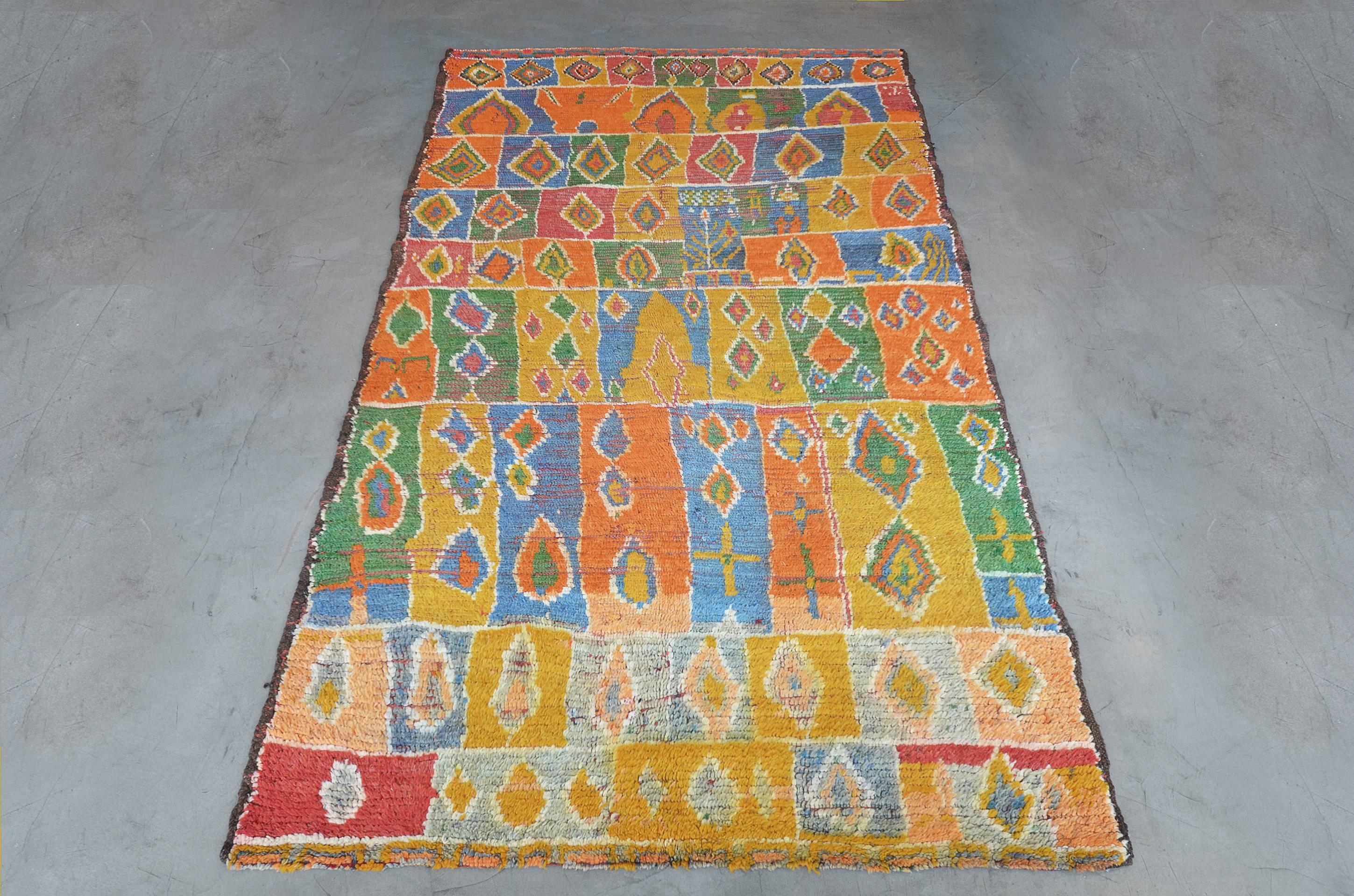 This vintage Moroccan rug features a field with an overall design of linked polychromatic square and rectangular panels of light grey, rust-red, shaded blue, burnt-orange, bottle-green and mustard yellow each panel containing angular floral motifs.