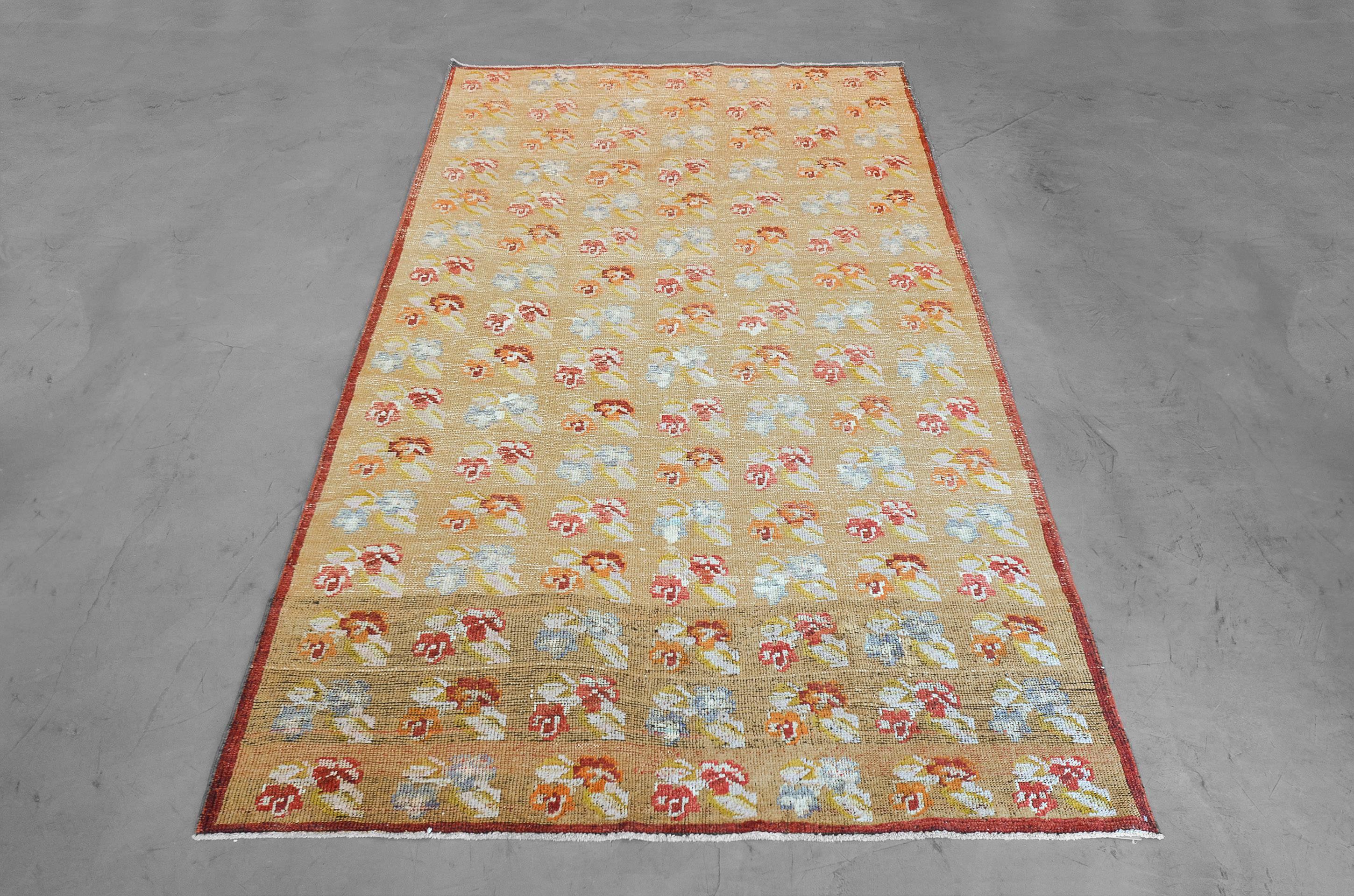 Vintage wool floral in warm tones worn to perfection, hand-knotted in Turkey in the late 20th century. An earthy red border acts as a delicate outline to this fashionable rug. Sized at 5’6 x 9’2” this rug works well for a small seating area or an