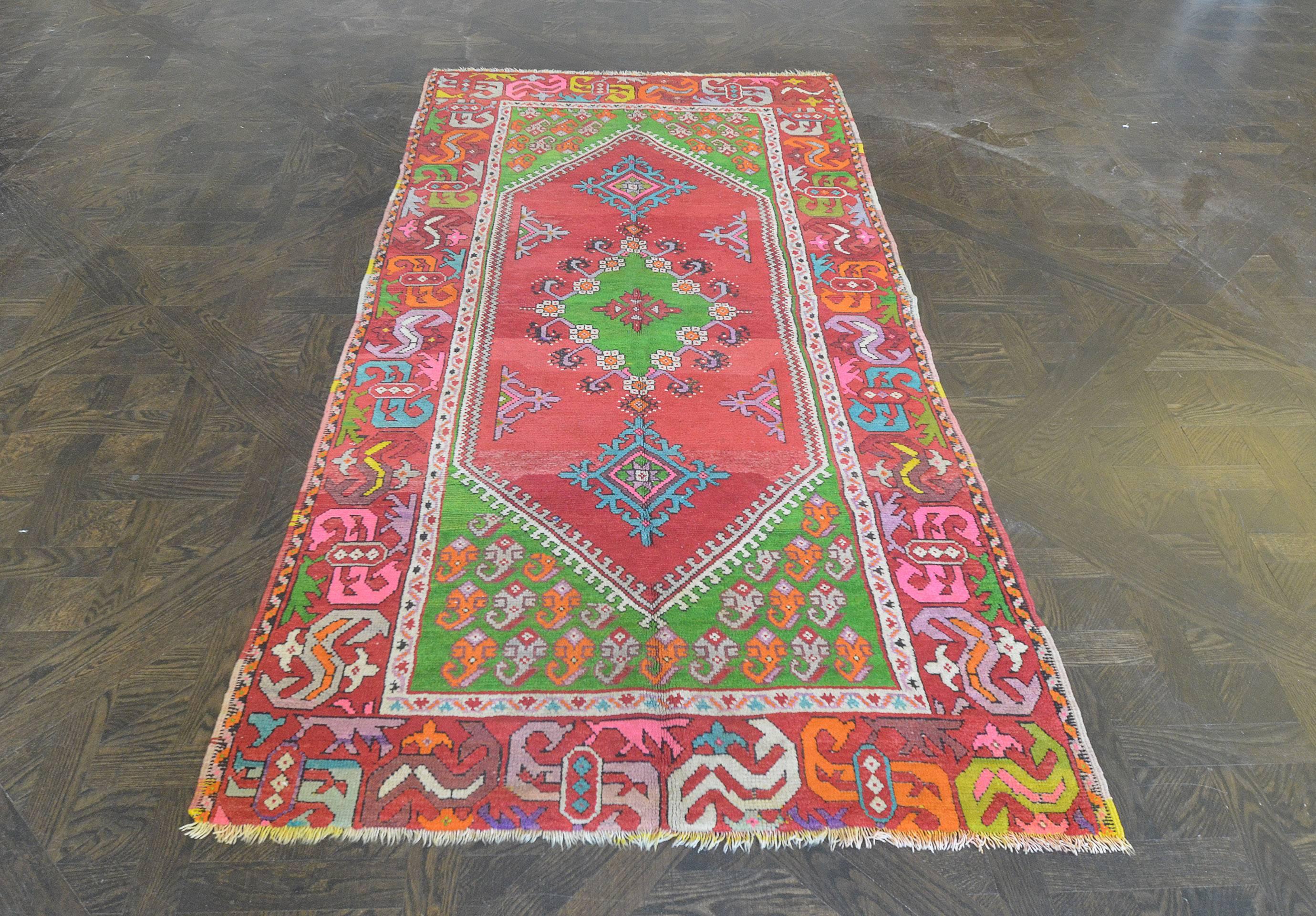 This traditional handwoven Turkish Ghordes rug has a shaded ruby field of angled floral lozenges and half lozenges, in an harlequin green hooked lozenge medallion, in harlequin green paisley spandrels, broad shaded ruby lozenge border of prismatic