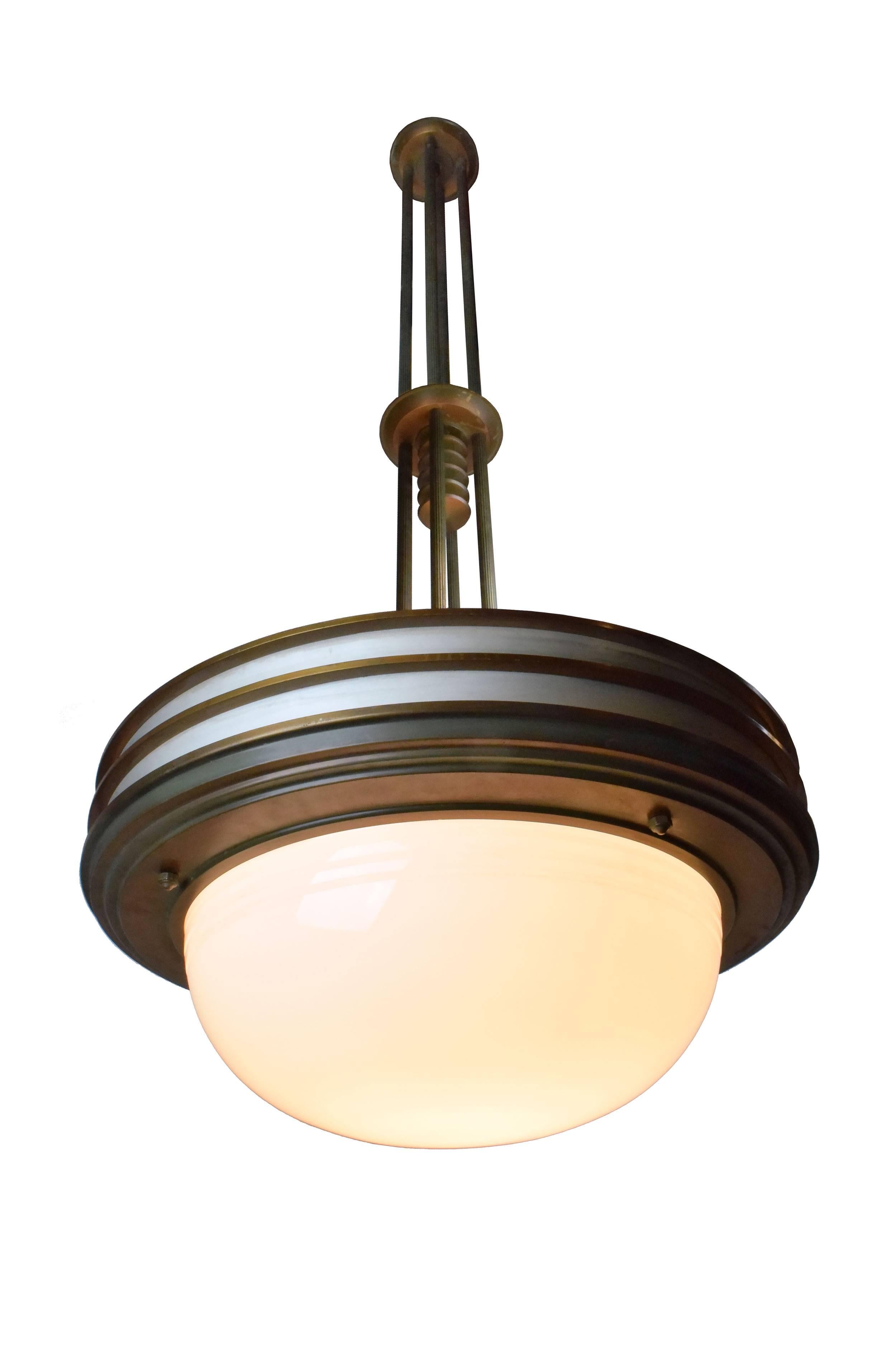 These incredible chandeliers epitomize the streamlined, geometric lines of the Art Deco movement. Four ribbed, cylindrical brass rods suspend each fixture over feet in the air and from these a tiered pendant holds a huge etched glass bowl in place. 