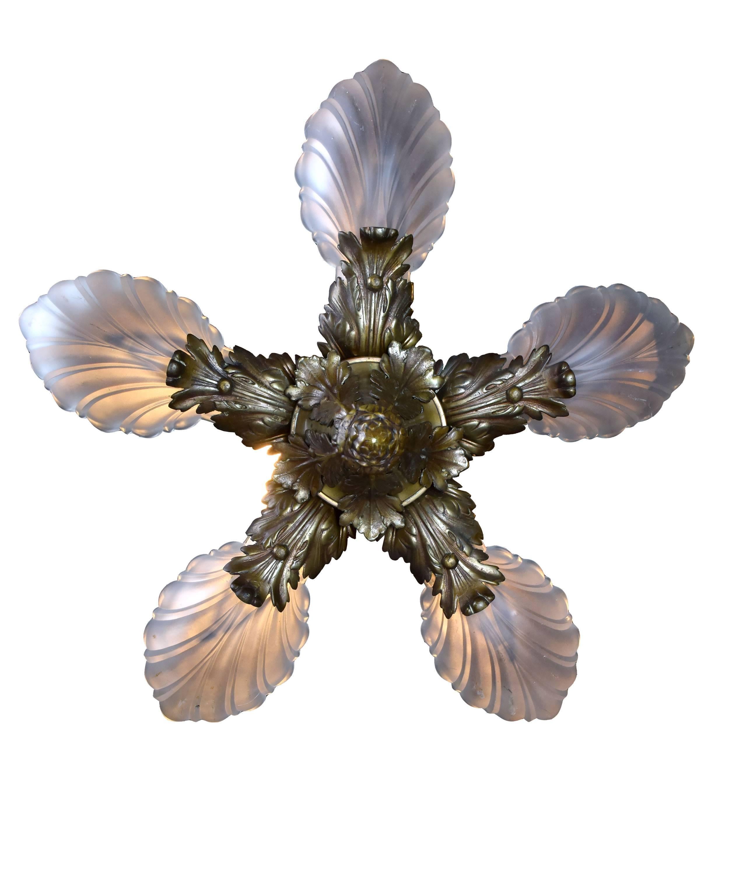 This incredible Art Deco brass chandelier features five opaque shades whose scalloped detailing beautifully matches the curving, leafy details throughout the fixture. Details abound; from the Classic pineapple finial to the scrolling details on the