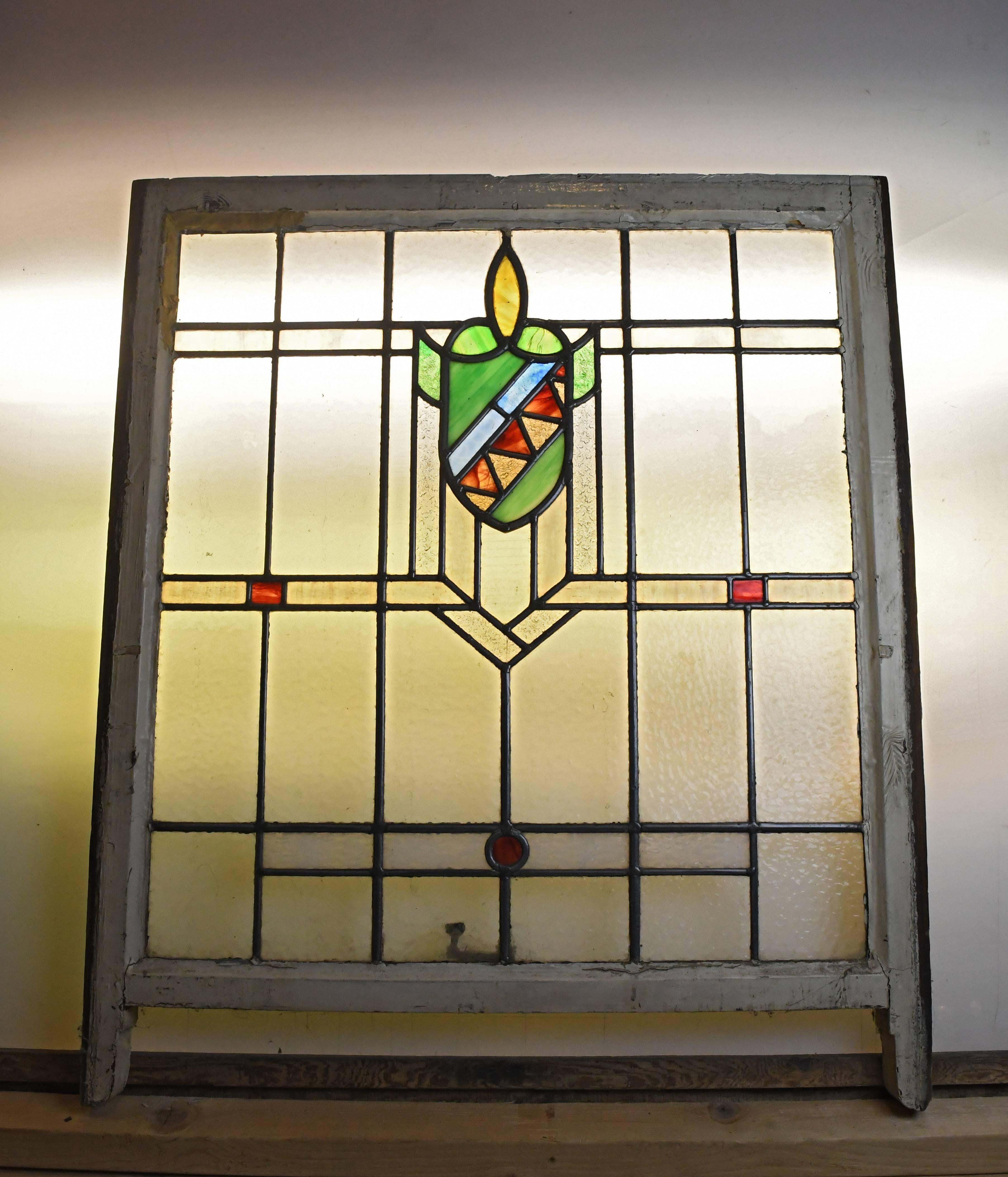 This wonderful stained glass window has various textured panels of glass throughout, small red glass squares, a small red glass circle at the bottom, and a beautiful shield design serving as the main focal point of the whole window. The colors on