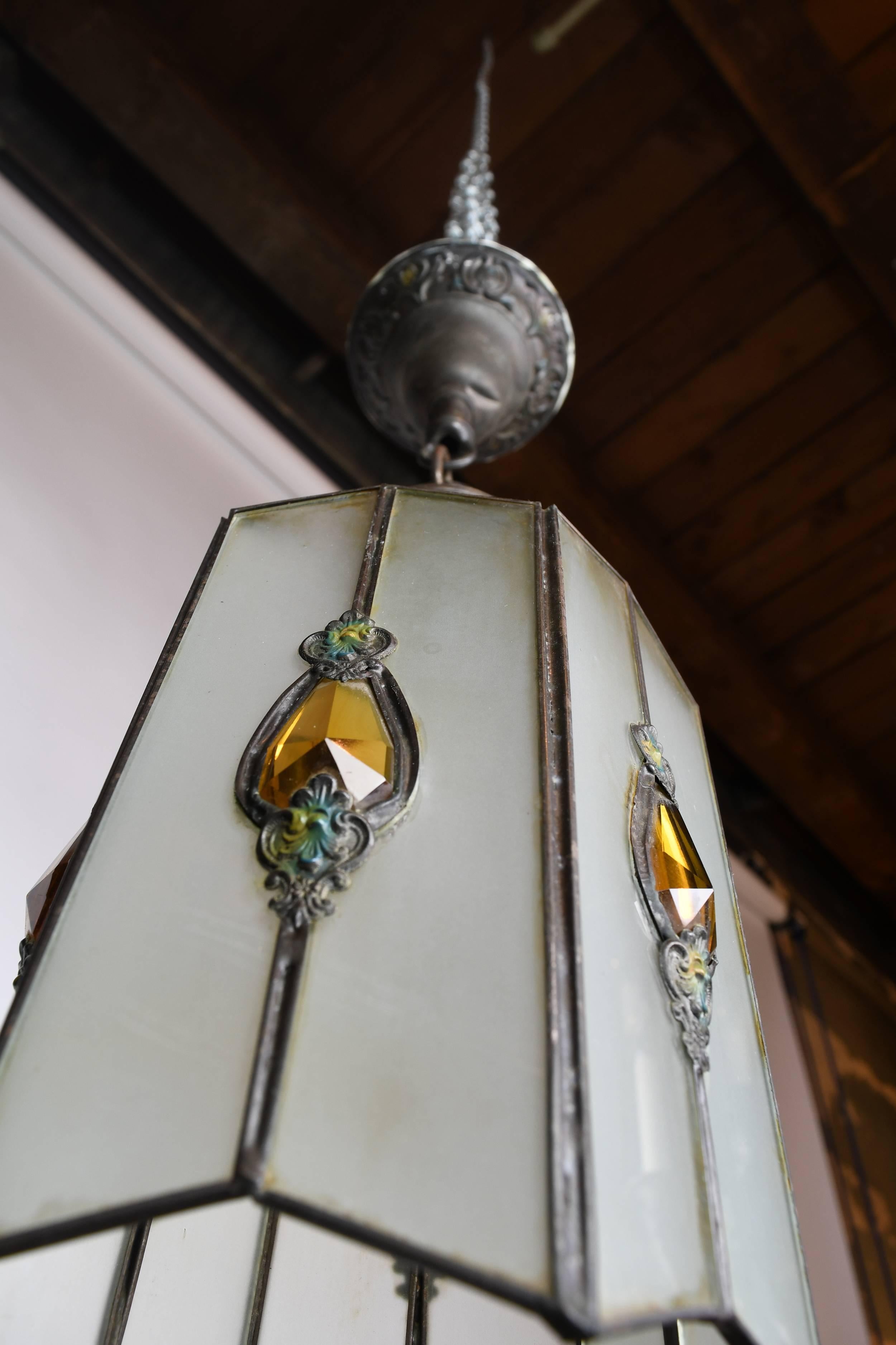 This pendant has a delicate, Arts & Crafts and Gothic influenced design, decorated with amber-colored glass teardrops on all six sides of the glass shades. The canopy and holder are ornamented with acanthus motifs.

We find that early antique