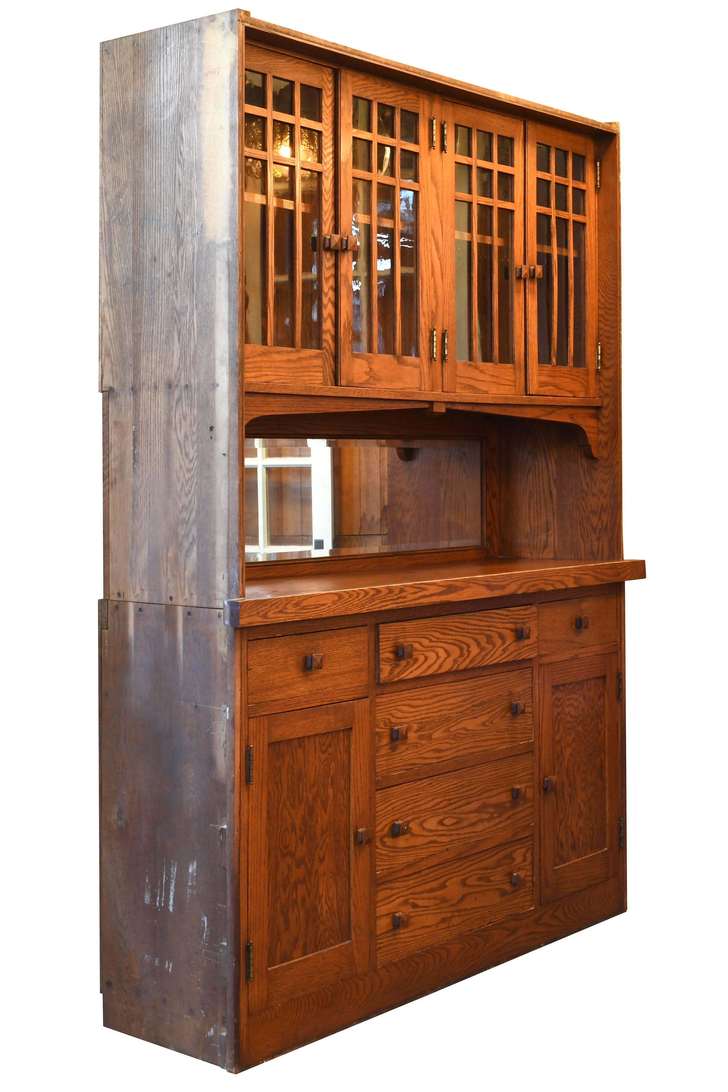 This buffet is classic and clean craftsman style at its finest. A long beveled mirror flanks the center; above it are two large cabinets with shelving, and below are additional cabinets and multiple drawers. The oak is warm in tone, lending the