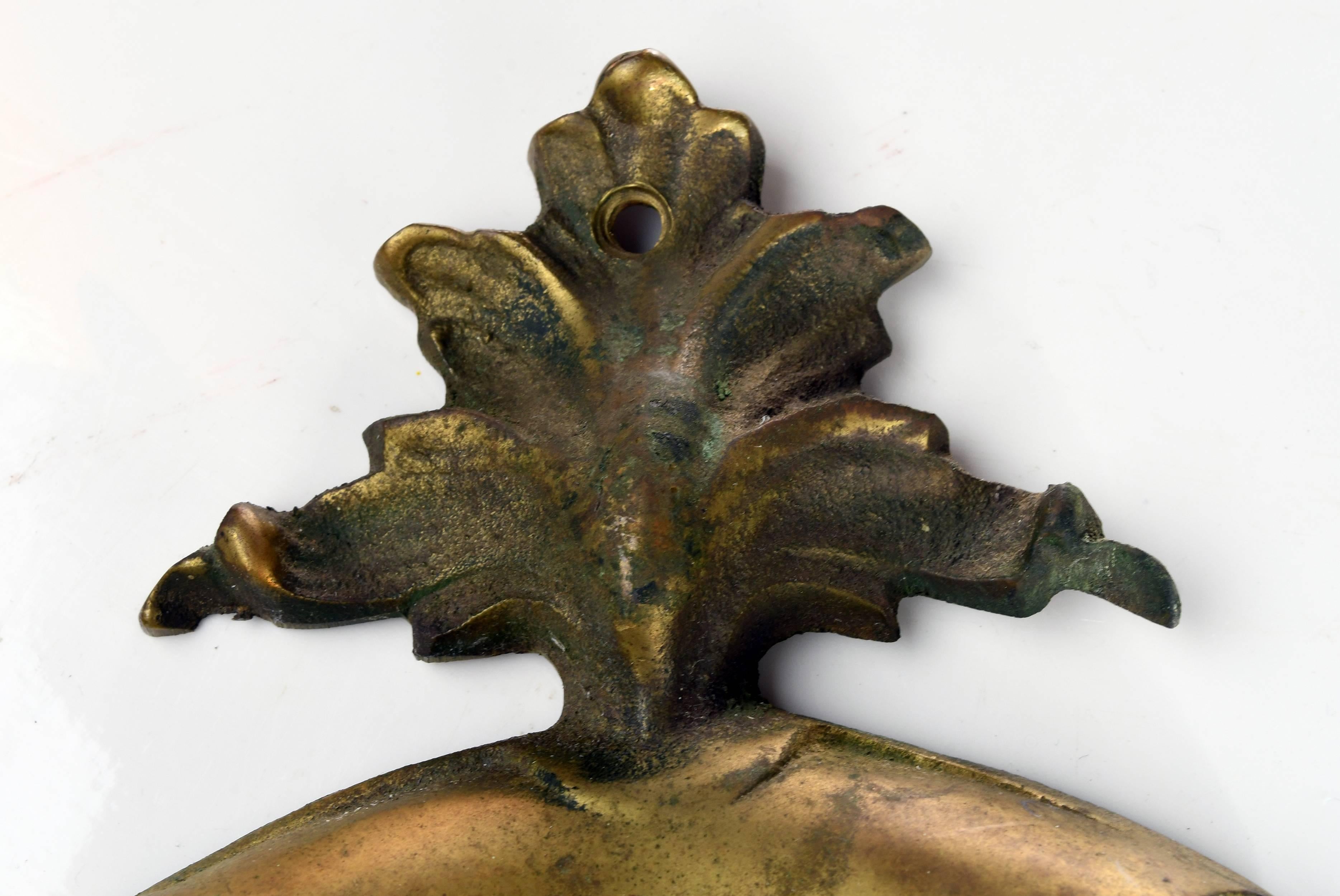 This cast brass door knocker is decorative and designed with floral elements. In the middle of the plate, the letter 