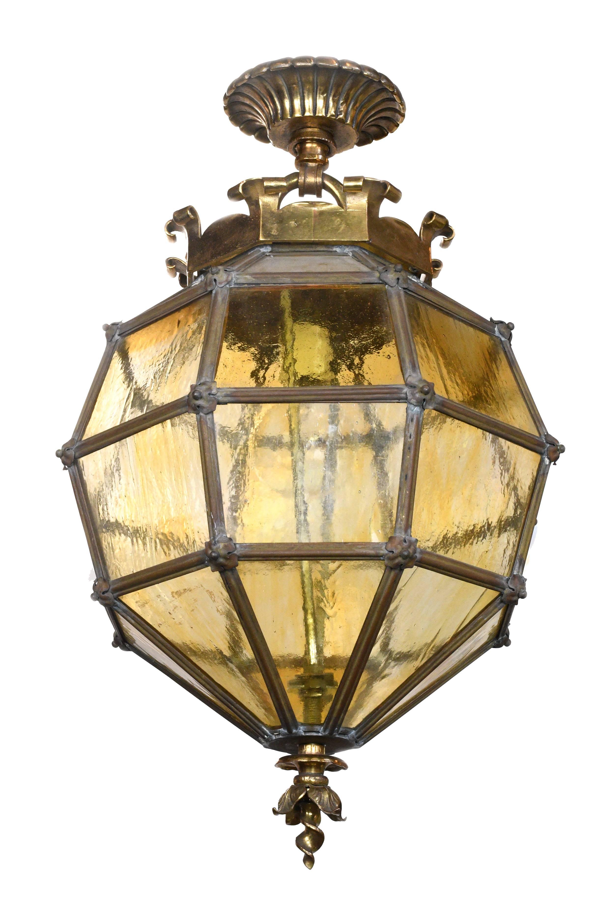 Thirty two yellow glass panels are arranged in an octagonal shape, lending this fixture a stylish, modern air. A cast brass, crown-like canopy adorns the top, and a leafy finial rounds out the bottom. Between each panel of glass is a delicate metal