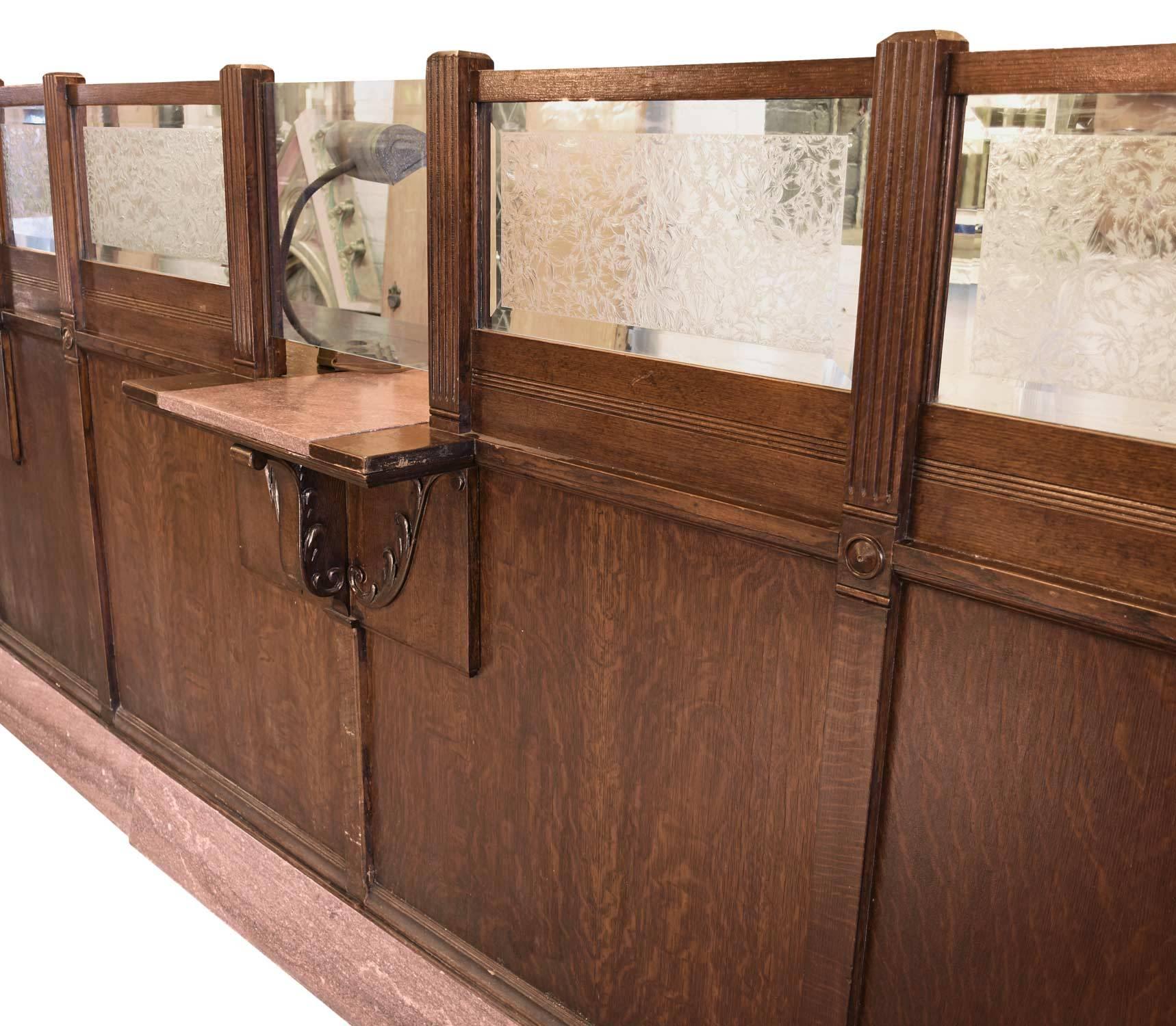 This original turn-of-the-century bank teller counter exhibits a lovely combination of materials, in oak, glass and granite.  On the front of the counter, two teller windows are created with clear glass and salmon colored granite and are surrounded