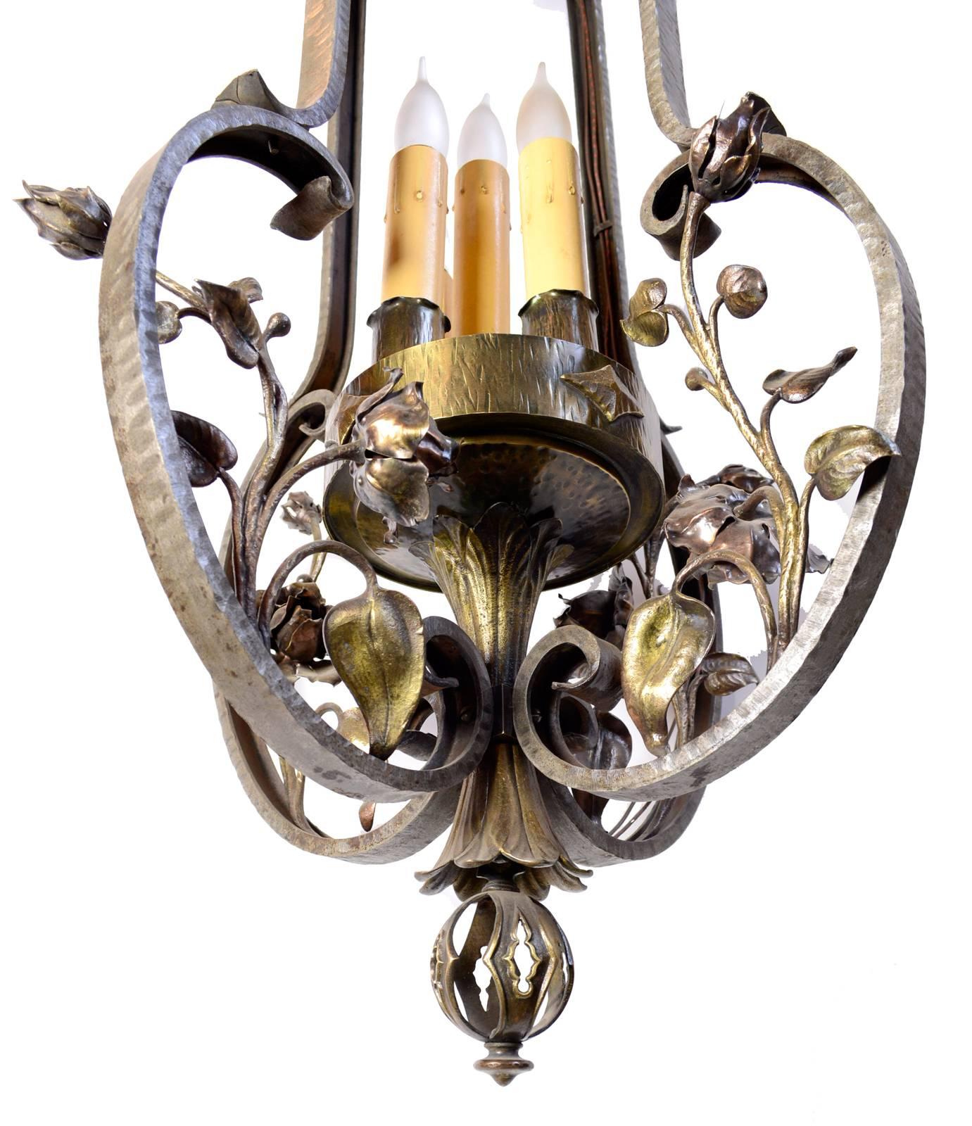 This amazing fixture features details and craftsmanship belonging to an era long past. A mix of hand-wrought iron and cast bronze creates the frame of this elaborate pendant, where organic vines are interwoven with the large bronze arms. An