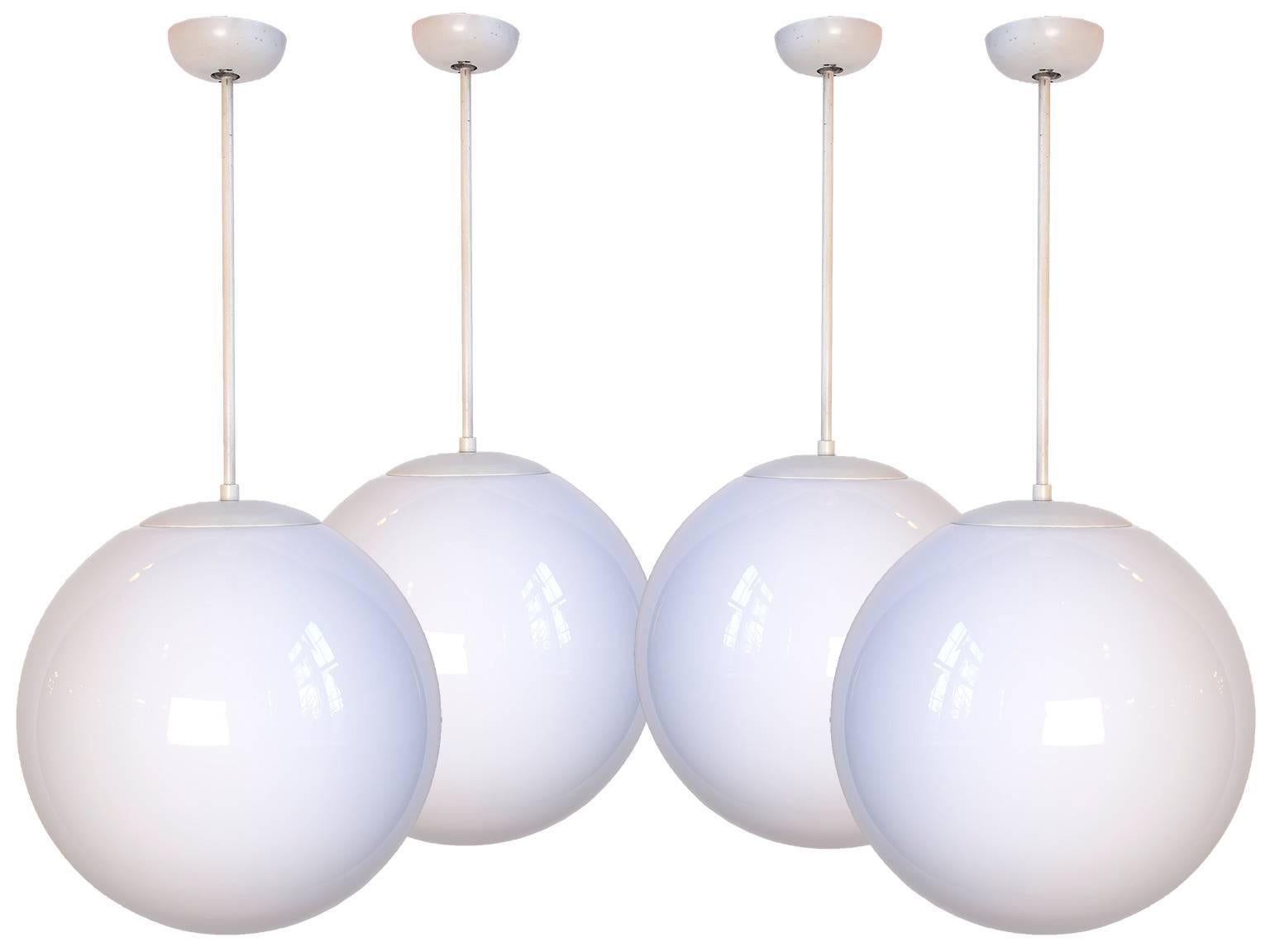 These fixtures are a streamlined and clean look from the early 1960's. Each fixture includes a milk glass spherical globe with an original pole pendant, fitter, and canopy. They look great hanging together in a running line or at staggered