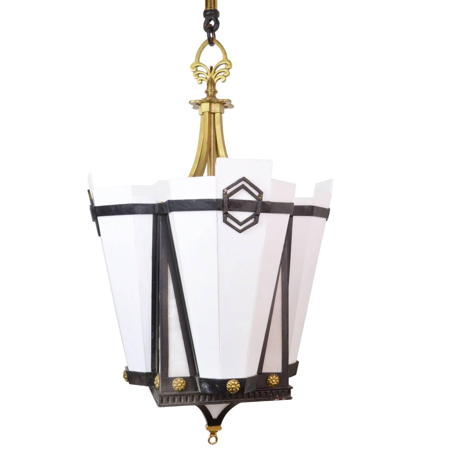 Made in the 1920s, these pendants are constructed from iron and brass and have interesting geometric milk glass panels. Other details include bent glass panels, an ornate chain, and geometric, Art Deco detailing throughout. Matching pair