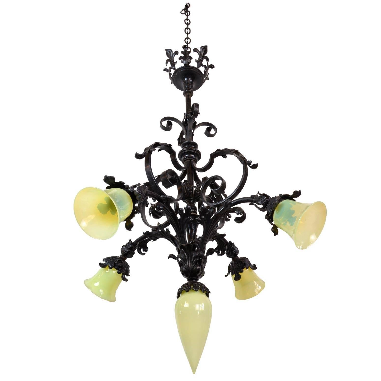 Made circa 1915, this iron chandelier has Gothic details, including scroll and leaf decoration as well as vaseline glass shades on each of the four arms and the center closed shade. A beautiful, ornate addition to a room in need of some historic