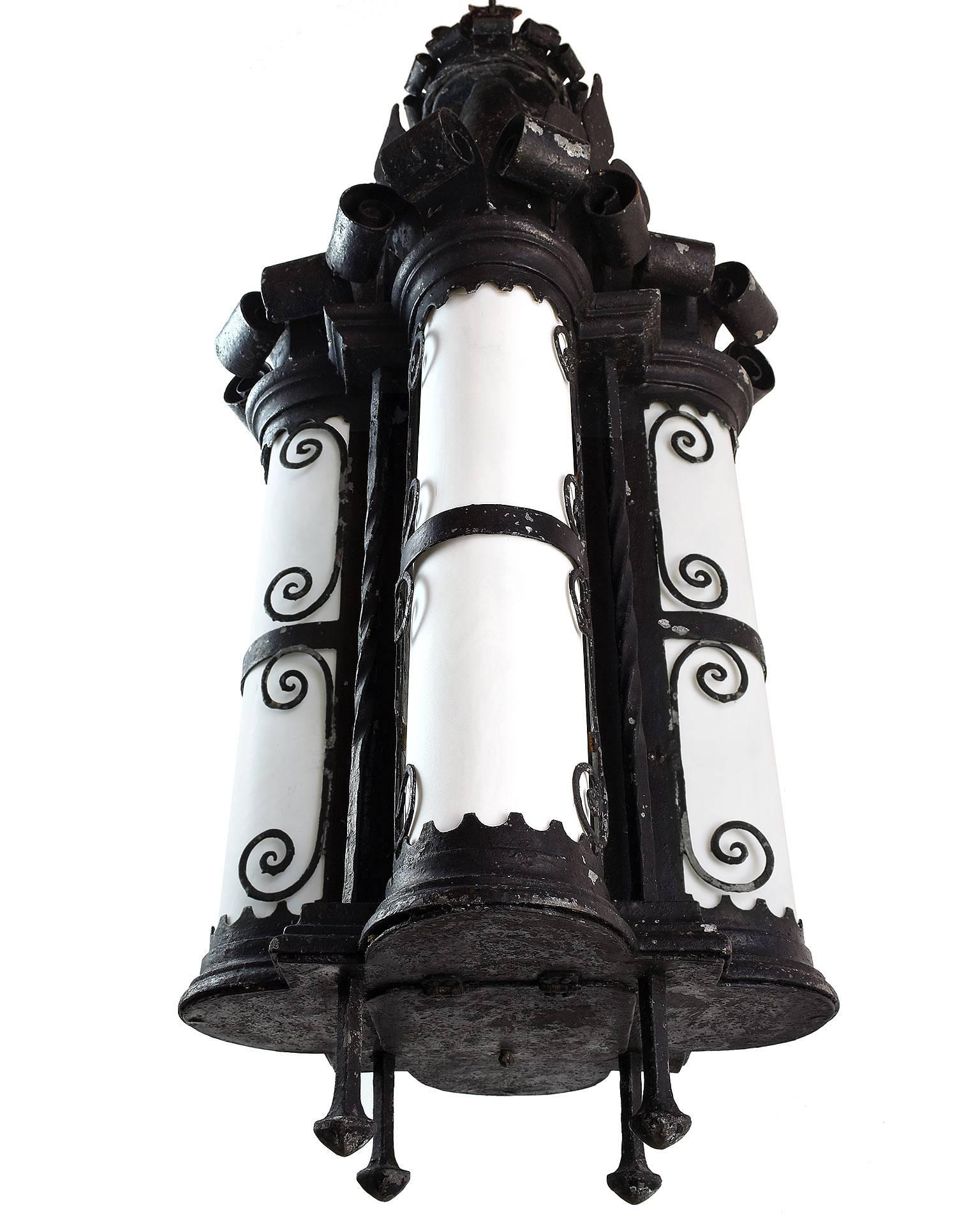 This large iron Gothic pendant is a complex combination of materials and shapes! The white opaque bent glass panels highlight the stunning silhouettes of the multiple ornaments, including fleur-de-lis, scrolls and castellations. A quatrefoil shape