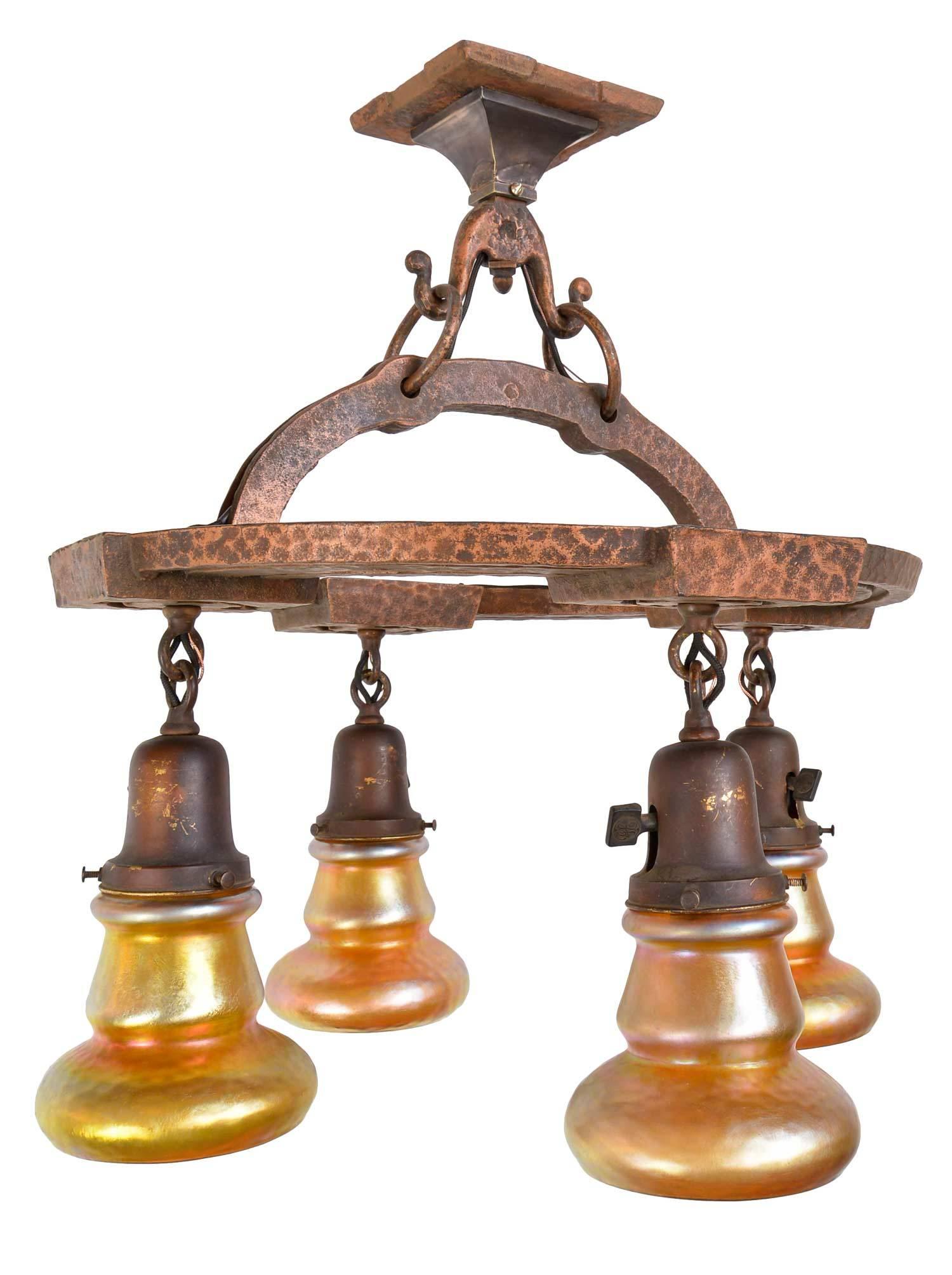 This is an exceptional turn-of-the-century Arts and Crafts cast iron, ring chandelier that includes an amazing set of Quezal shades, unusual in shape and finish. This light is an impeccable example of Arts and Crafts lighting with a wonderful