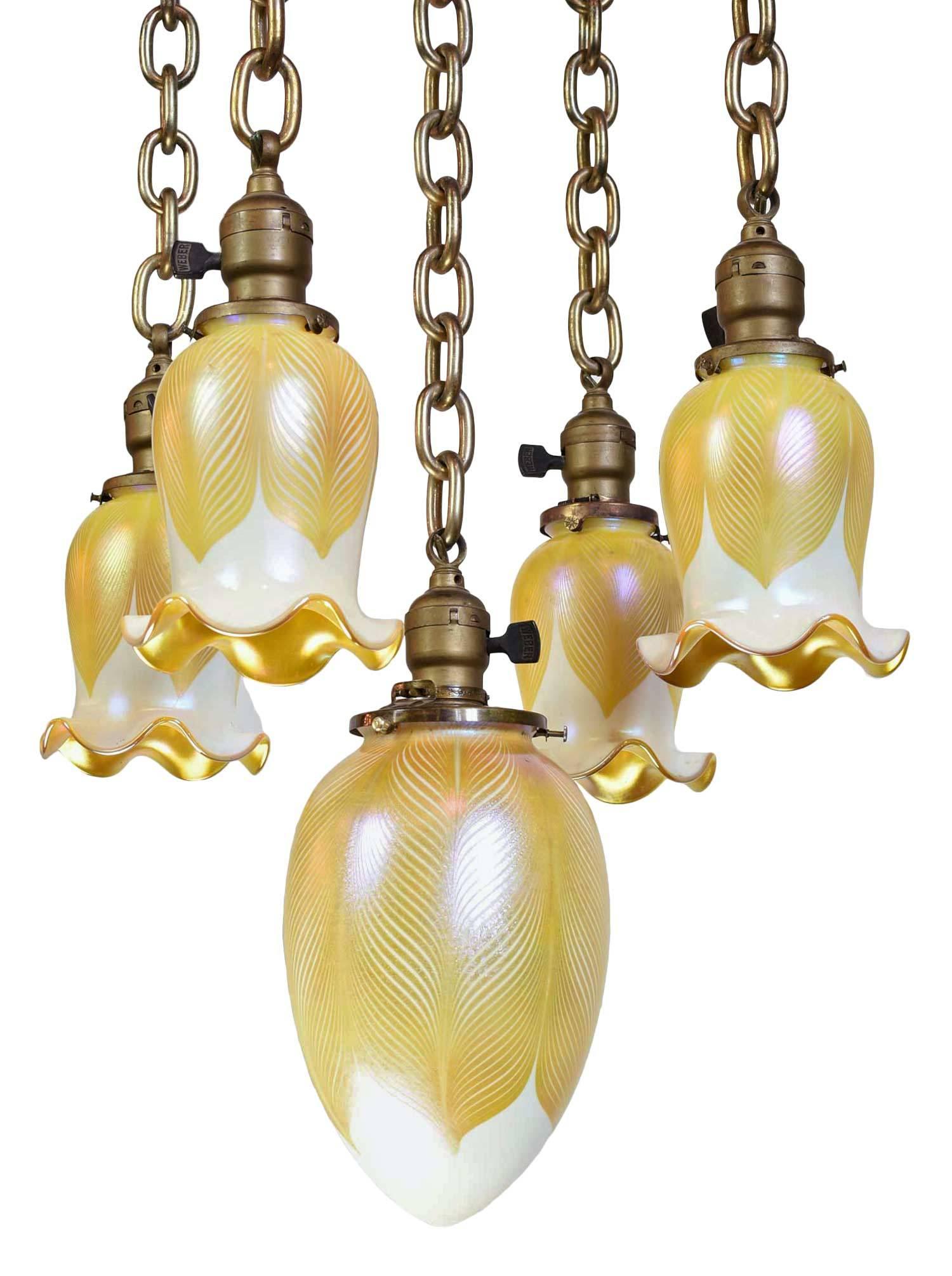 This set of Quezal shades are a great example of early American art glass. Each shade is signed and in pristine condition with a loverly iridescent Aurene finish and pulled feather pattern. This cast brass fixture has a flushmount pan with five