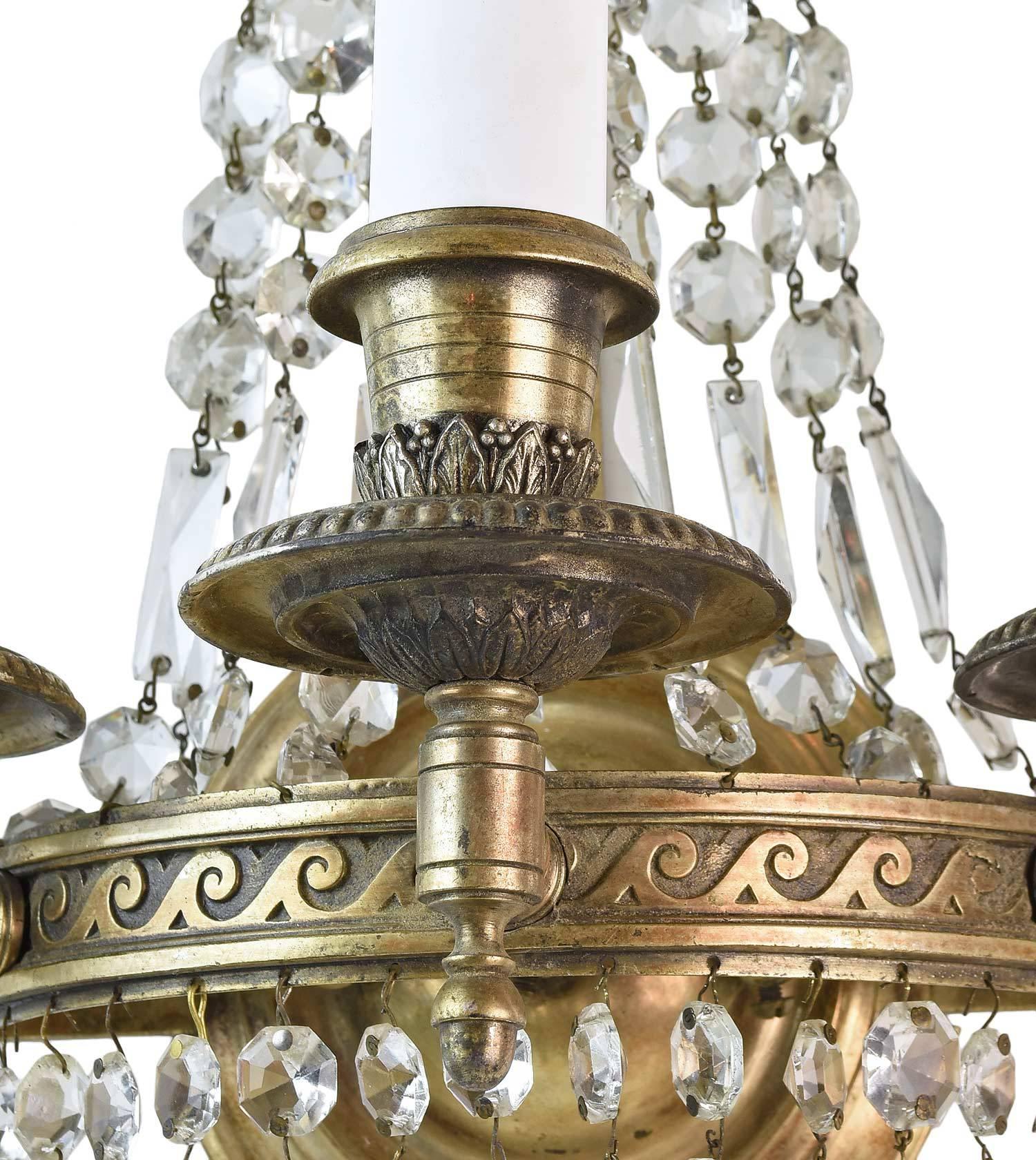 A neoclassical design from the 1930s, this is a stunning over-sized three-candle cast brass sconce with decorative crystals along the back and bottom. The sconce has ornamentation throughout, with  scroll details in cast brass, leaf detail, and an