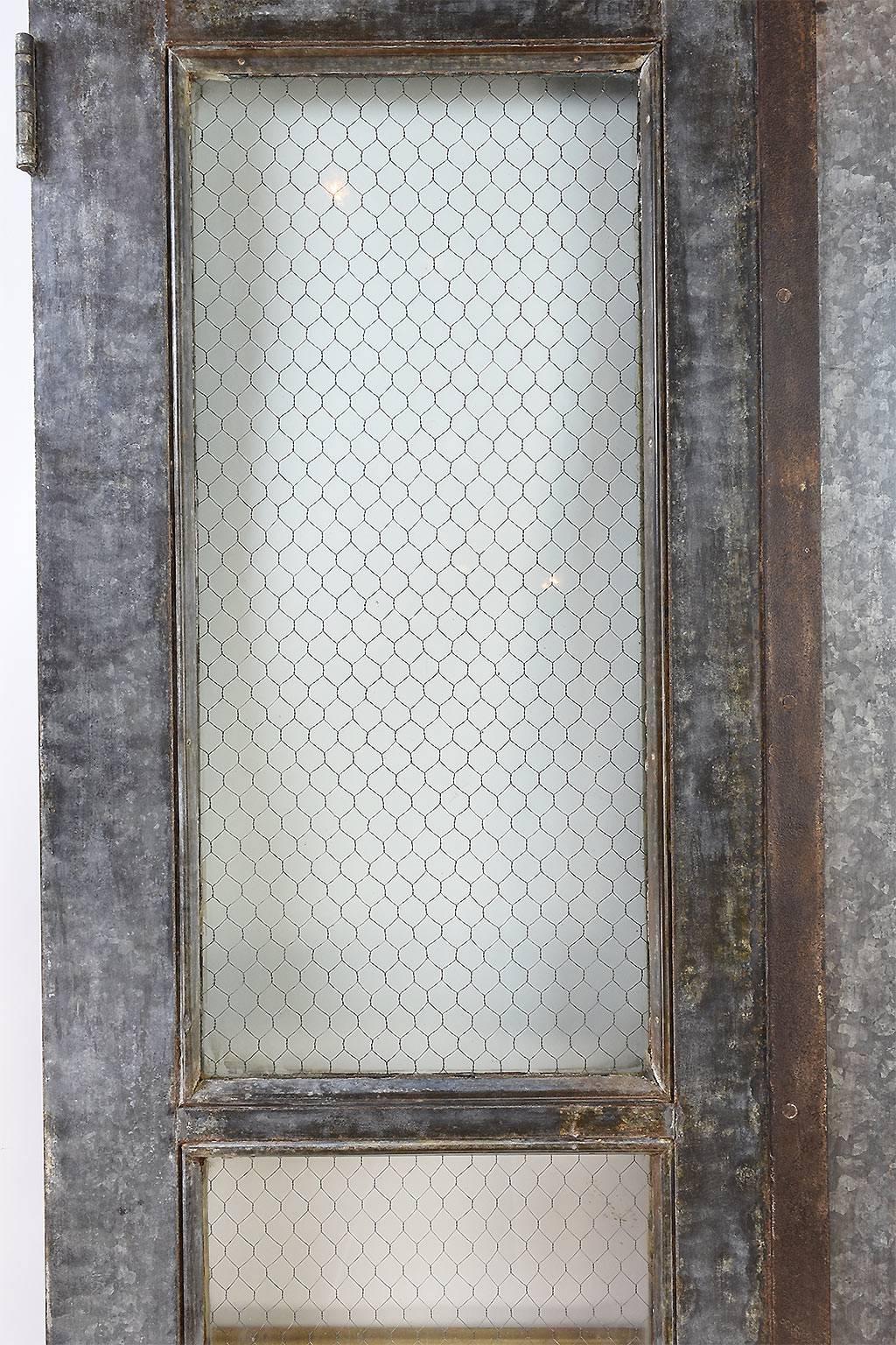 Saved from a school in eastern Ohio, this set of double doors is the epitome of the 'Industrial door.' Clad in galvanized tin, each door has chicken wire glass making up the full-view windows. Additionally, made in 1910, the doors are complete with
