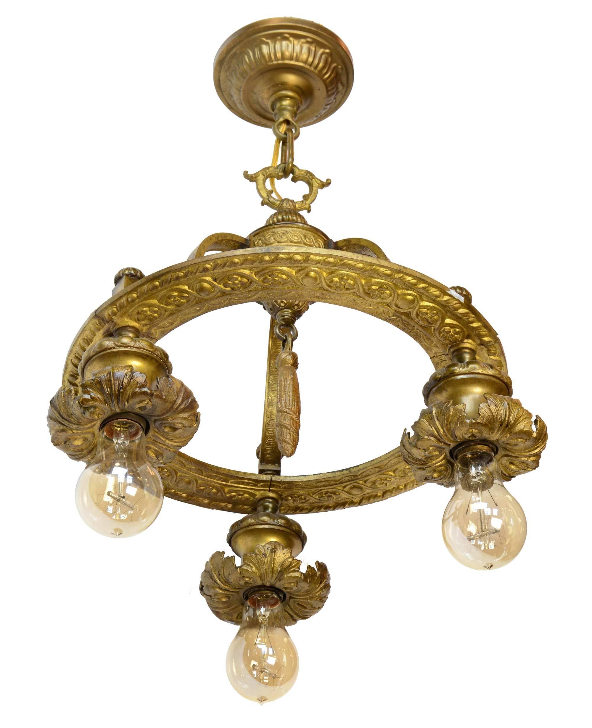 A highly ornamented cast brass ring light with Beaux Arts-style decoration, including floral and acanthus leaf detail, acorn finials, and a rope tassel in the center. This beautiful fixture, inspired by the French Beaux Arts movement, has three