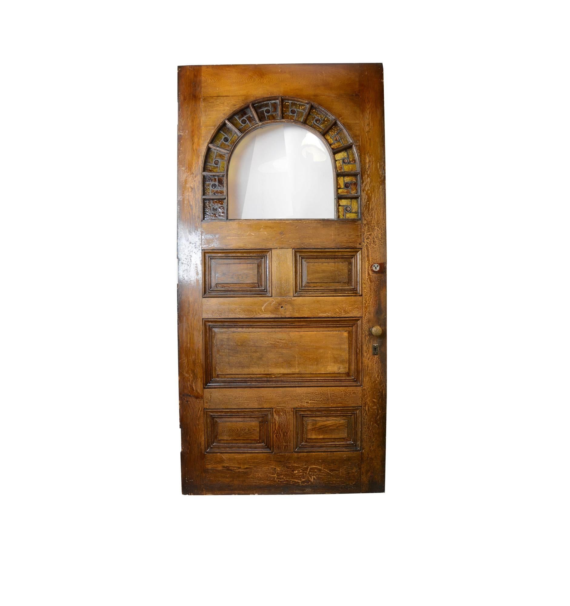 Made circa 1880, this solid oak door makes for an impressive entrance to any space. Standing at 8 feet tall, the door features an arch with beautiful amber-colored stained glass and red jewels. Decoration covers much of this door, as the top of the