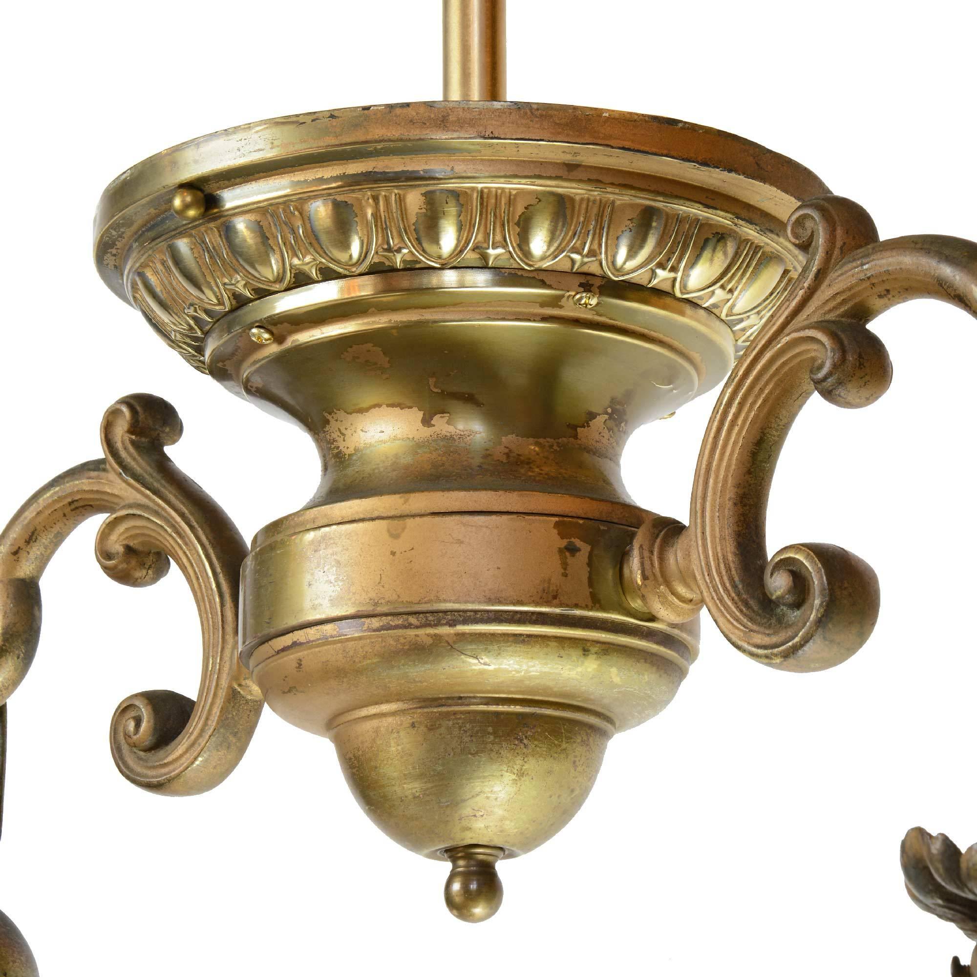 This brass fixture features two decorative arms with leafy fitters holding iridescent cut-glass antique shades, and a unique urn-shaped body with egg and dart detail, attributed to the Charles Polacheck & Brothers Company of Milwaukee,