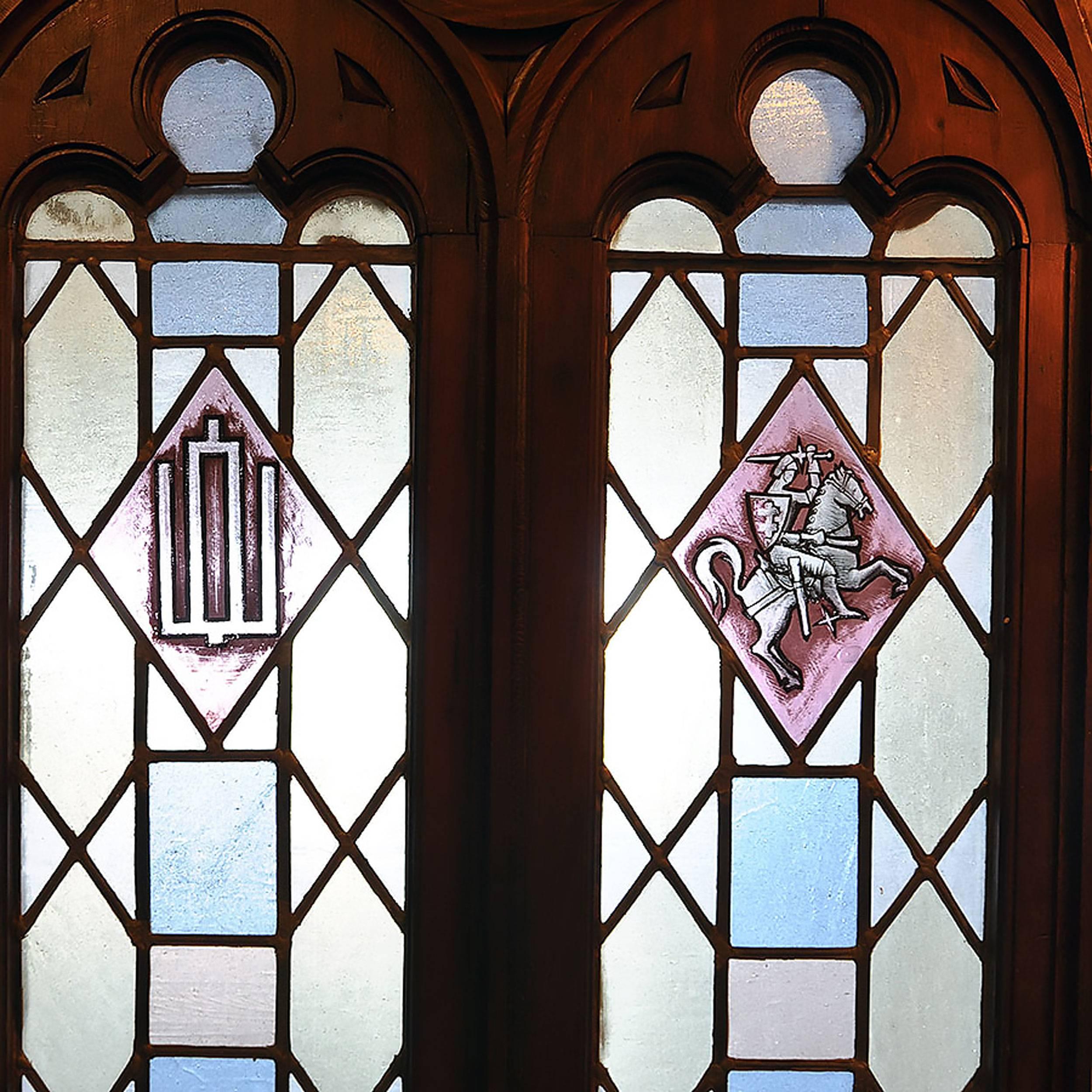Arched Gothic window with hand-painted emblems and stained glass in a variety of pastel colors. These window is encased completely in a heavy wooden frame. 

Window pictured: 96” tall x 40” wide.