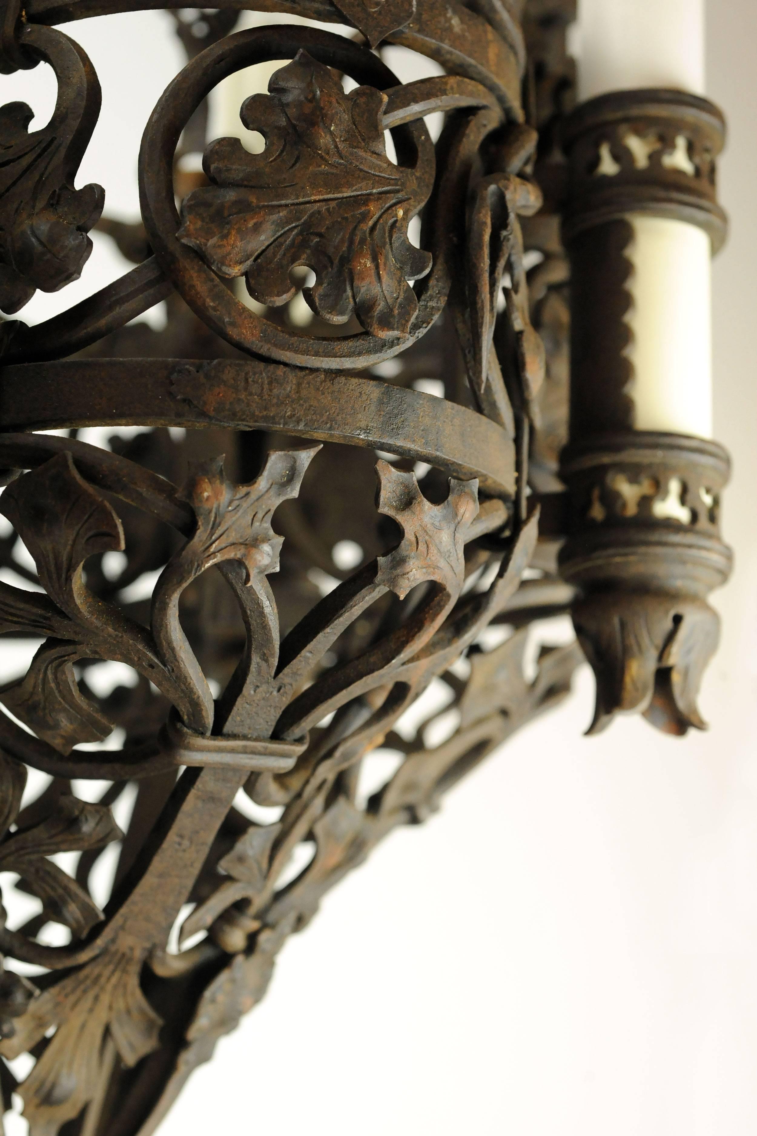 This wrought iron Tudor chandelier is truly a feast for the eyes. Leaves of varying shapes and sizes wraparound the fixture, giving it an organic, earthy feel, accentuated by thick strands of twisting, coiled iron. The four candle covers sit atop