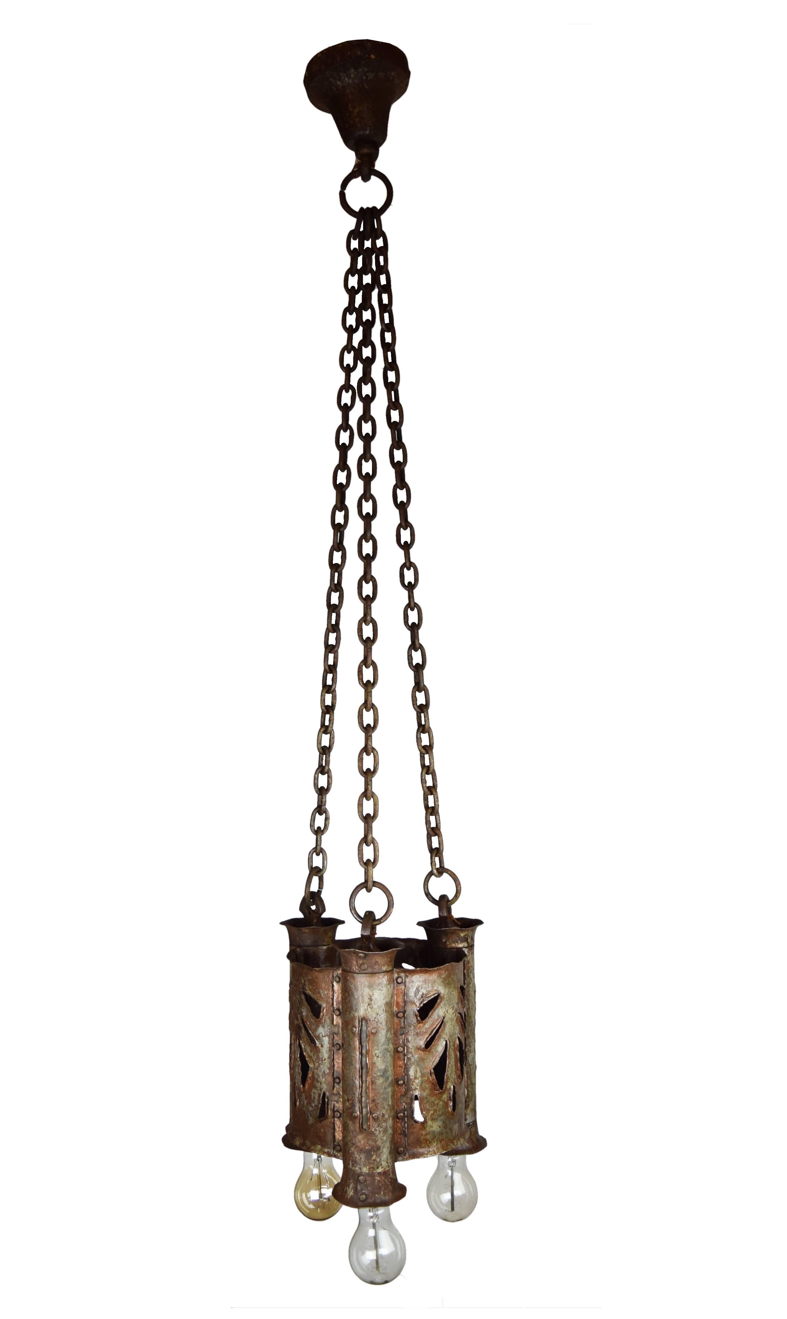 This wonderful Gothic iron three-light cylindrical pendant feature a unique cut-out design on all three faces of the fixture, a beautifully textured and hammered finish throughout, and its overall unique shape, style, and look would make them a