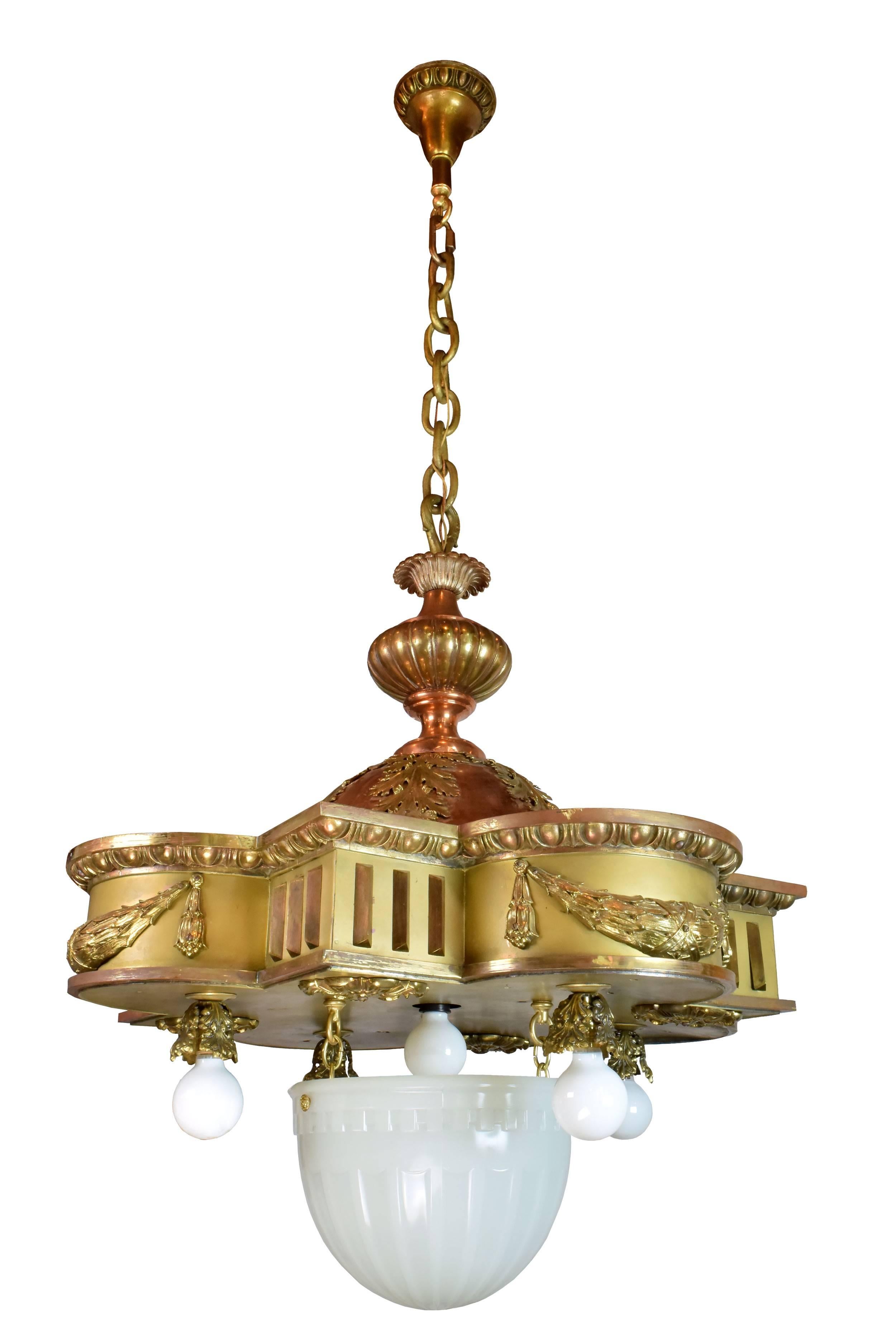 This gorgeous copper and brass theater light features a dazzling barbed quatrefoil base, which is adorned with large, ornate leaves and intricate garlands. Four bulbs hang from the bottom, surrounding an elegant ribbed bowl in the center. A thick,
