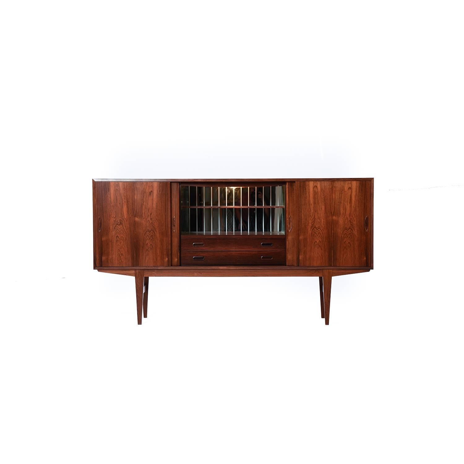 This stately rosewood credenza makes a statement open or closed. The center of the piece contains a self lighting bar with a pair of felt lined drawers. The side cabinets include generous storage with adjustable shelving.