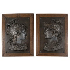 Pair of patinated metal bas-reliefs on a wooden display stand, 19th century.