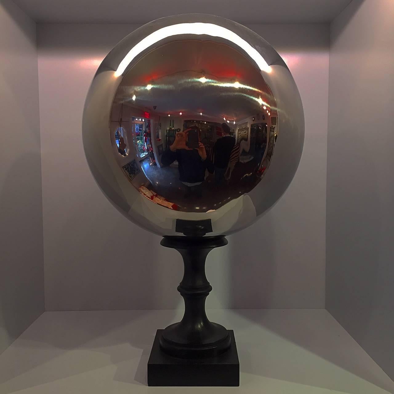 A stainless steel 'butler's ball' mounted on a turned wooden base. Butler's balls are used in dining rooms for the butler to survey the progress of a dinner party by looking into the reflection the ball placed on the side board without having to