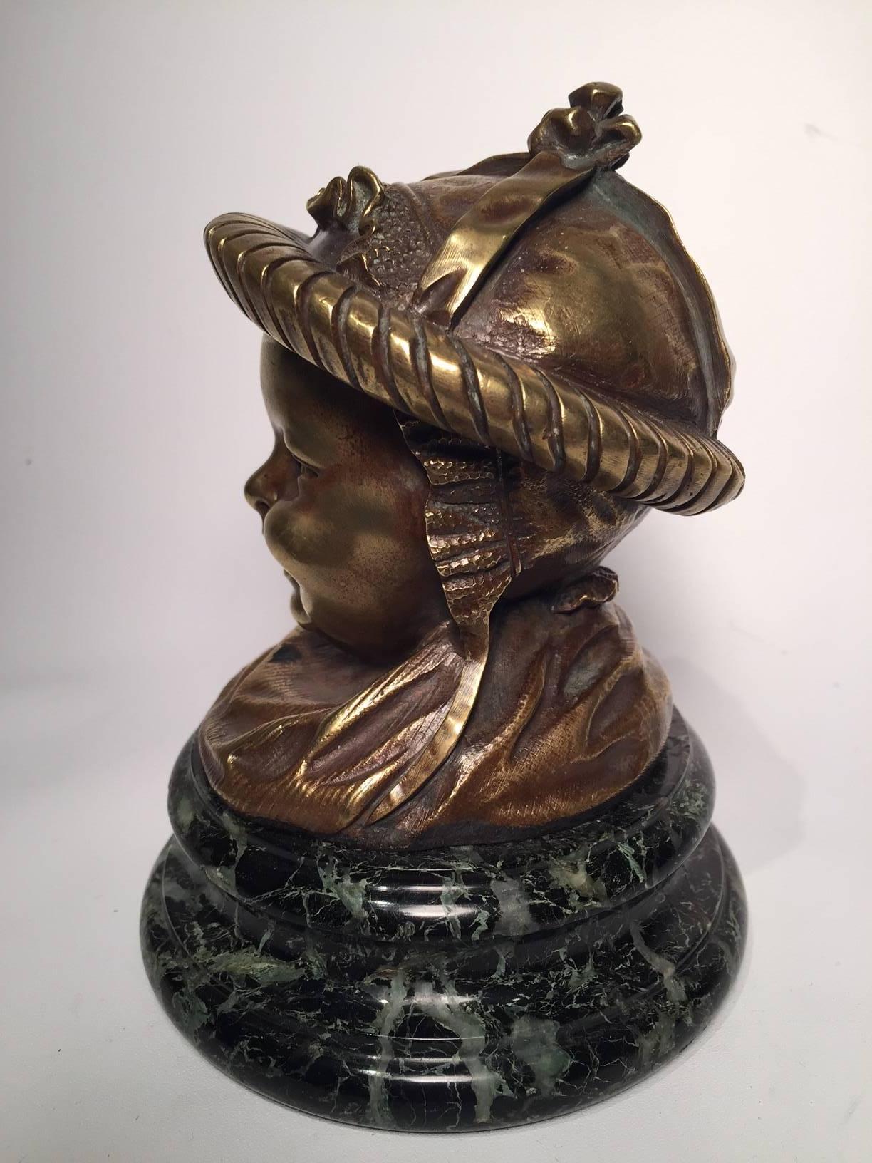 19th Century French Bronze Inkwell of a Baby on a turned green variegated marble base. This charming bronze was probably cast in the late 19th century when Orientalism was very much in vogue as the ribboned baby's bonnet seems to be inspired by East